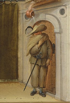 Image of a man in baggy clothing, cape, and wide-brimmed hat standing by a door having a pitcher of water poured on his head