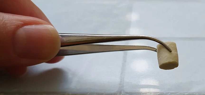 Photo of a hand holding a pair of tweezers that is picking up piece of ceramic