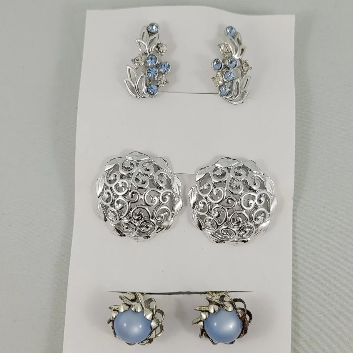 Three Pairs - 1950-60's Rhodium Domed Swirl Filigree and Inset Blue Moonglow Clip-on's and Blue Clear Rhinestone Silver Leaf Screw-Back Earrings