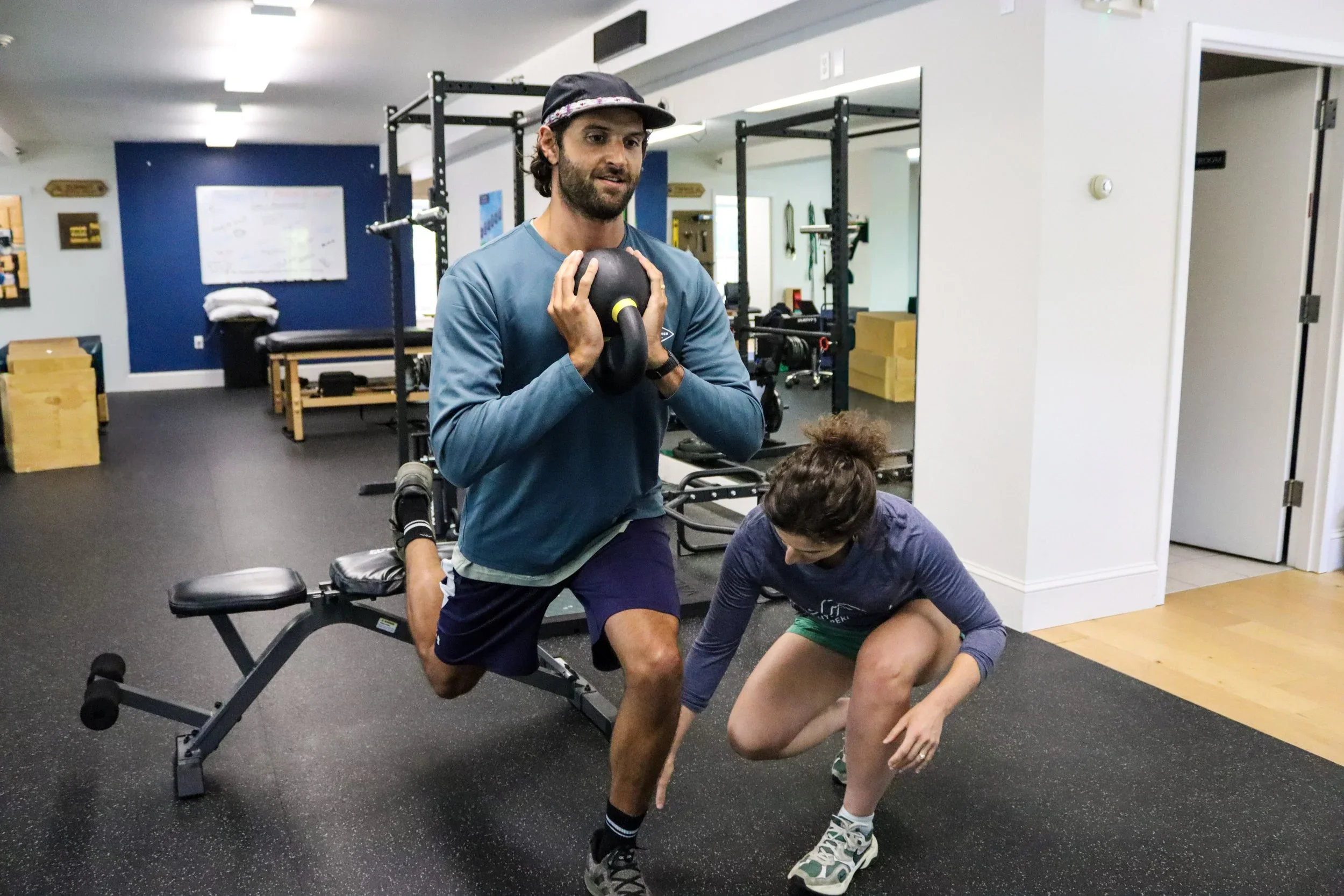 A man doing a squat with one leg on an exercise bench and the other on the floor holding a kettle bell