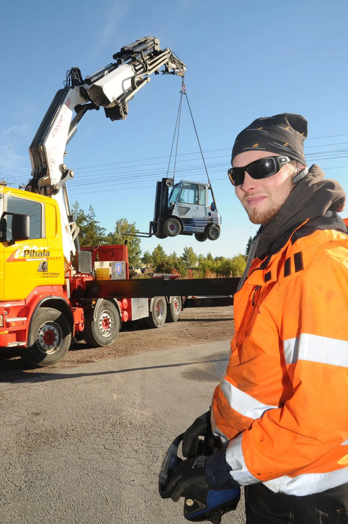 Pihalan kauko-ohjainta tottelee 110-tonnimetrinen nosturi, jonka taakkana killuu 4 500 kiloa painava trukki.  Lue lisää palveluistamme ⟶  Nosturit ⟶