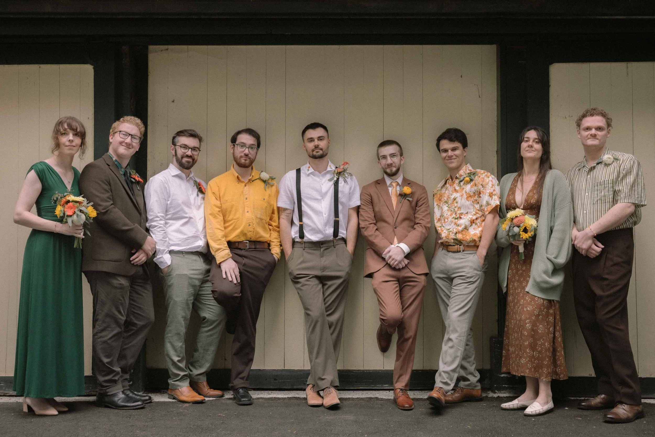 A groom stands with his groomsmen wearing yellow, green and brown wedding outfits.