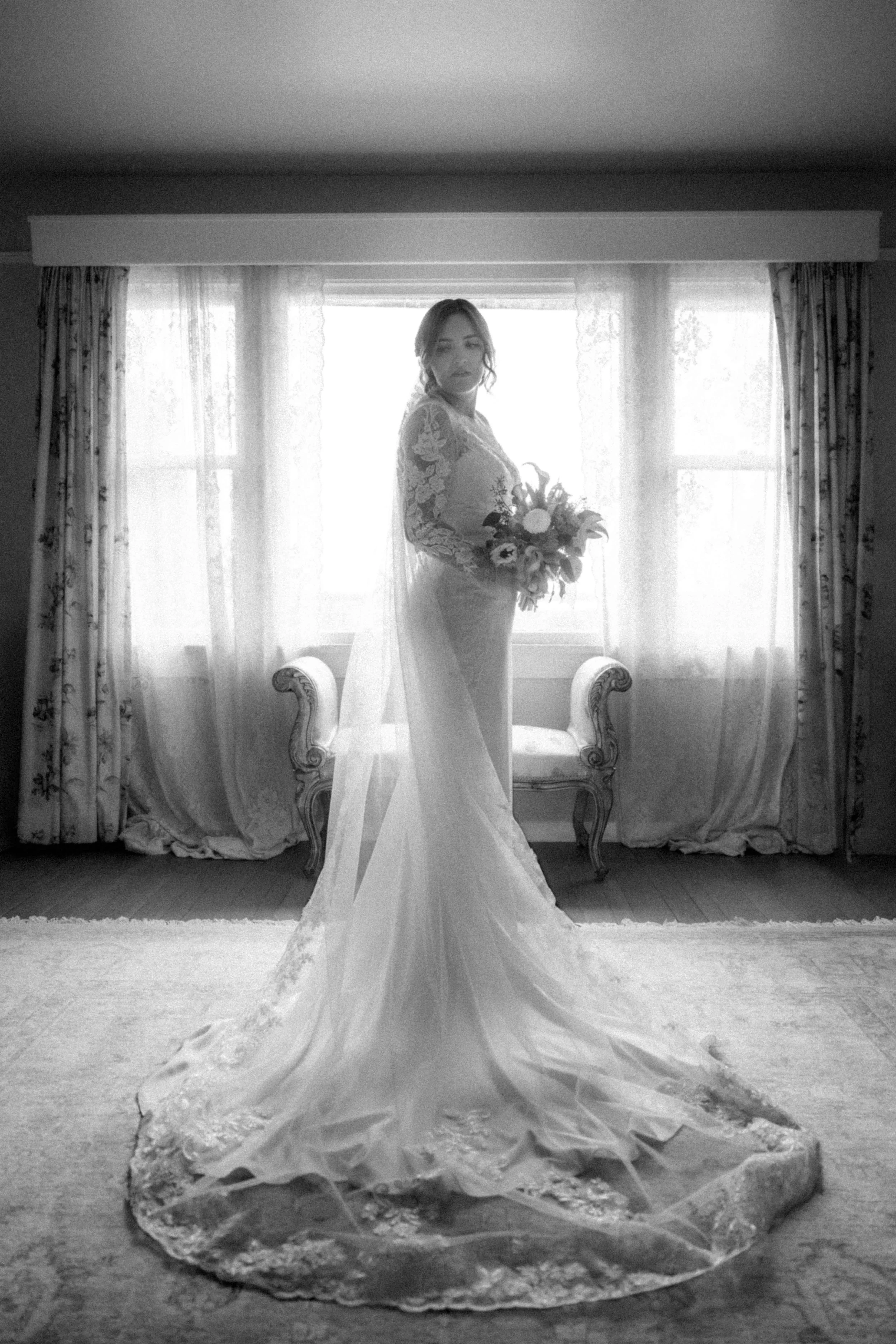 A black and white image of a bride wearing a long sleeved lace dress at the Minnekhada Lodge.
