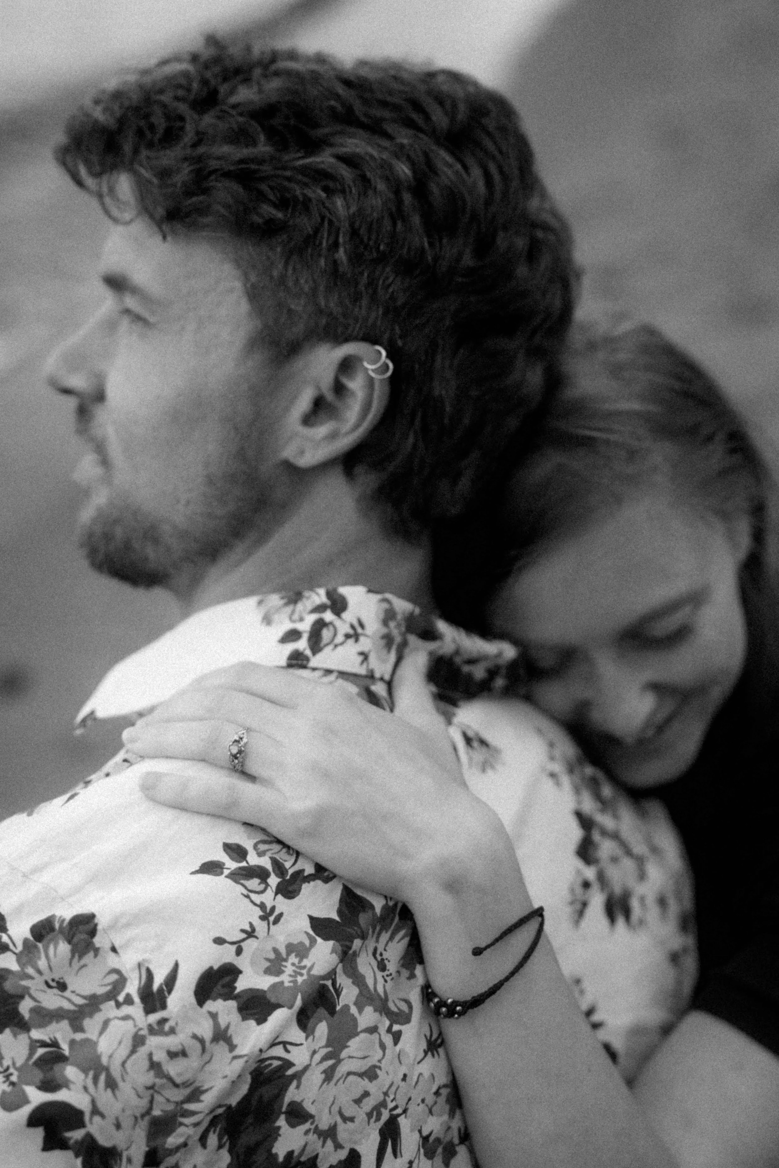 A black and white image of lovers holding each other on the beach with her engagement ring as the focal point.
