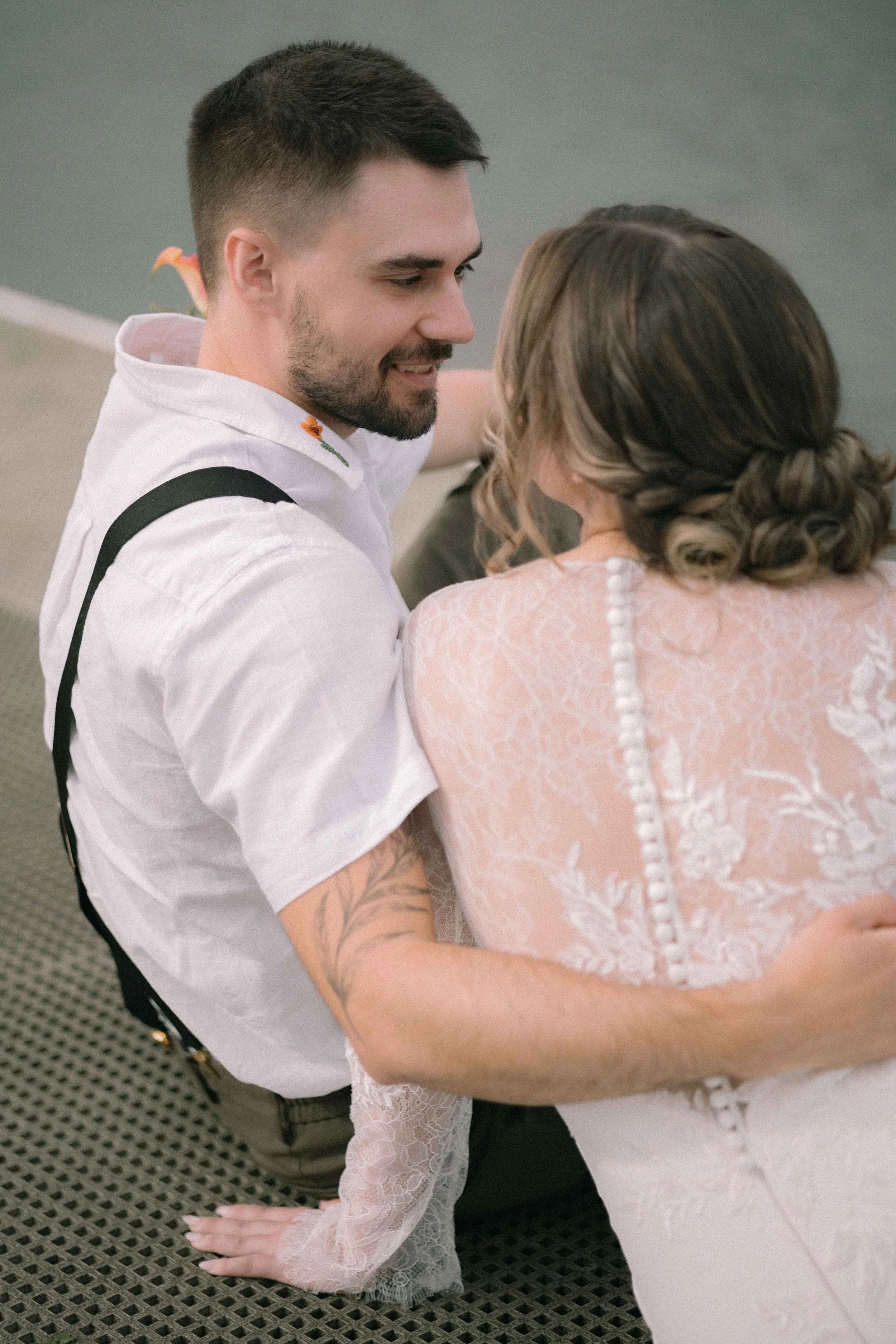 A groom with a white floral embroidered shirt holds his bride with a low cascading updo on the dock at Burnaby Lake Pavilion