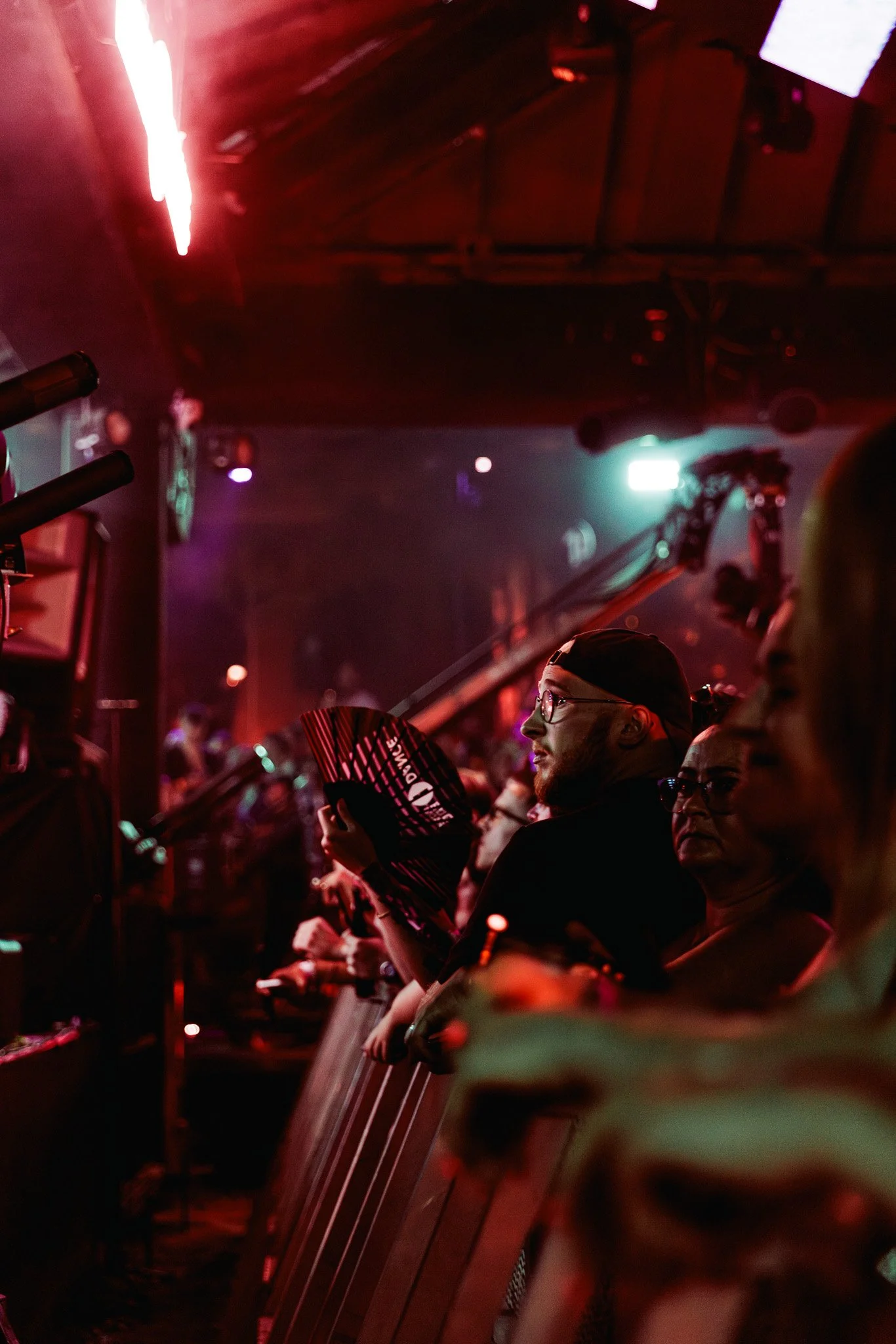 People sitting at a bar or club, holding fans, with colorful dim lighting and dark surroundings.