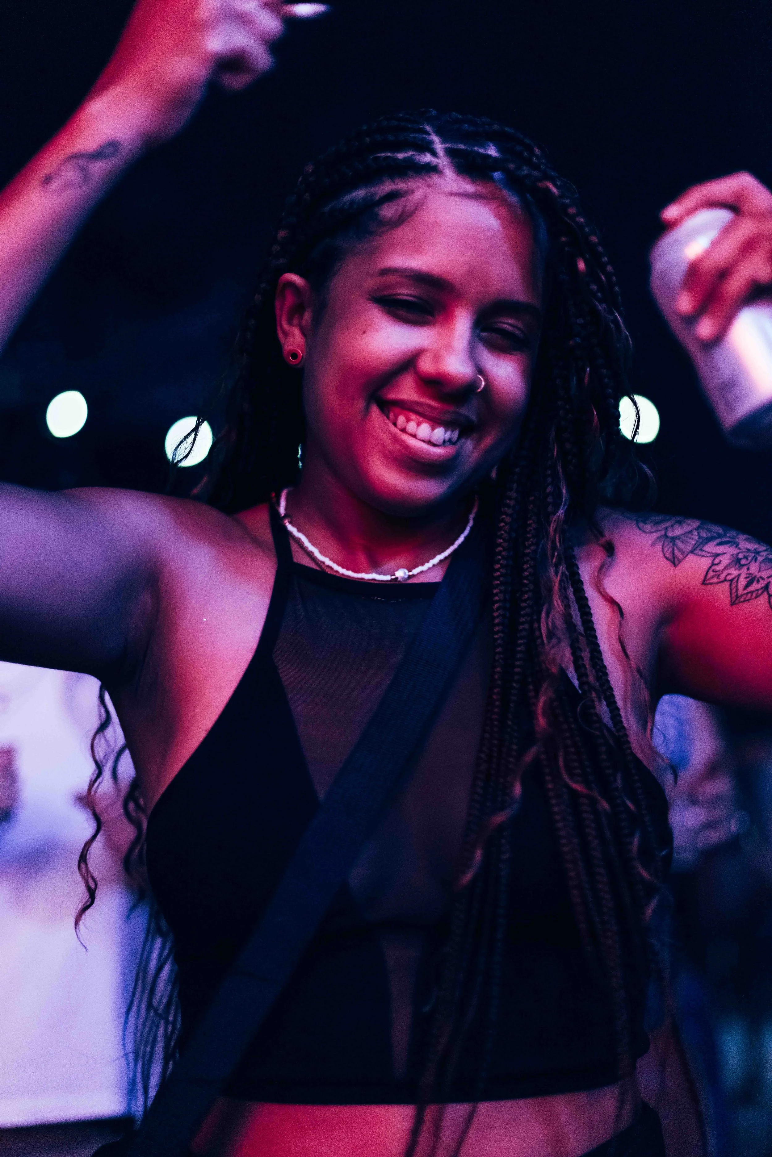 A young woman with braided hair smiling and sticking out her tongue, holding a spray can in her right hand.