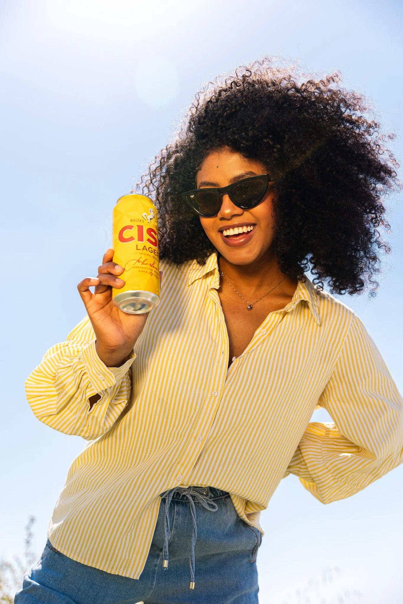 woman with big curly hair, outdoors, holding a cisk lager can