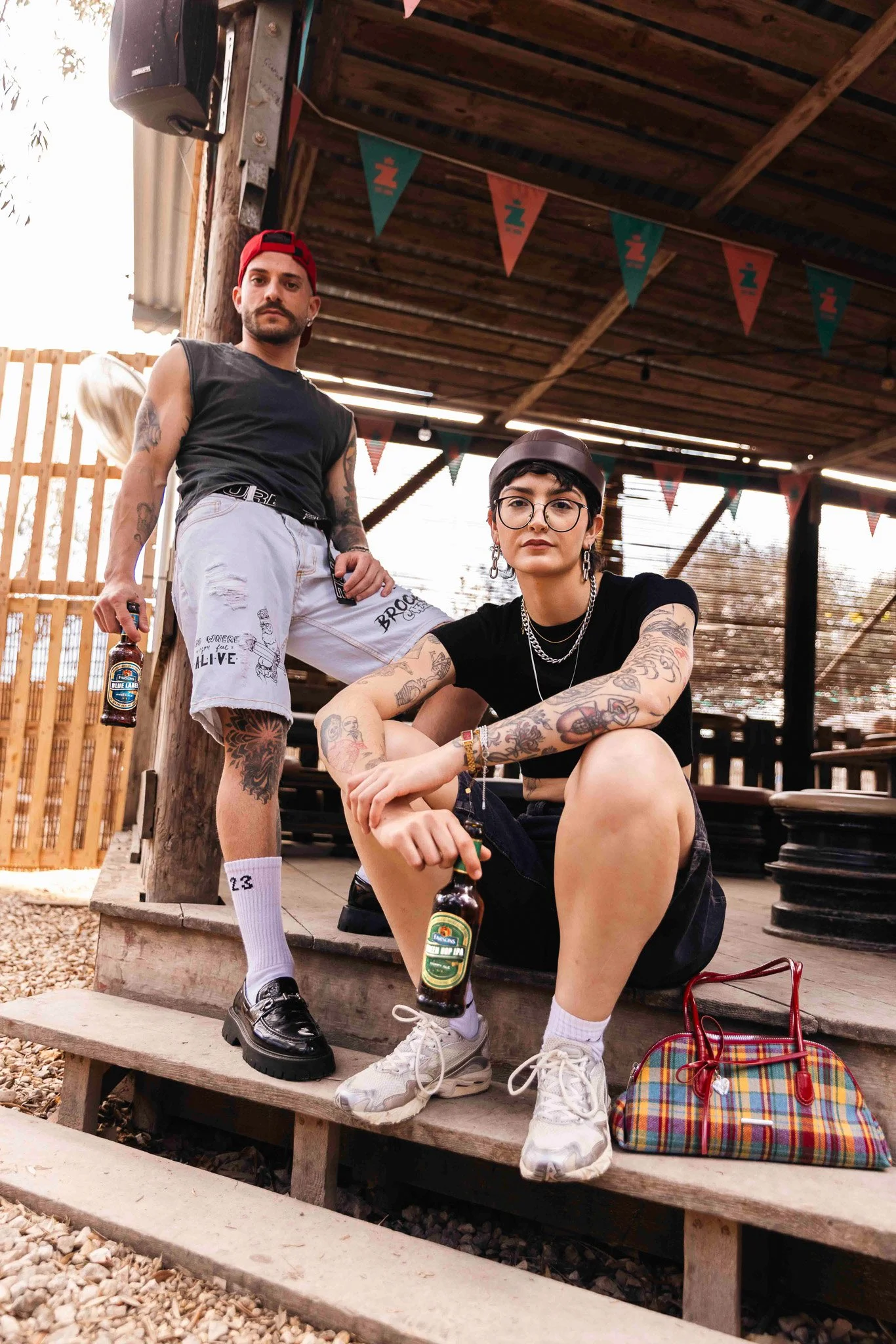 two cool, alternative models, holding classic brews beer bottles, outdoors, photoshoot