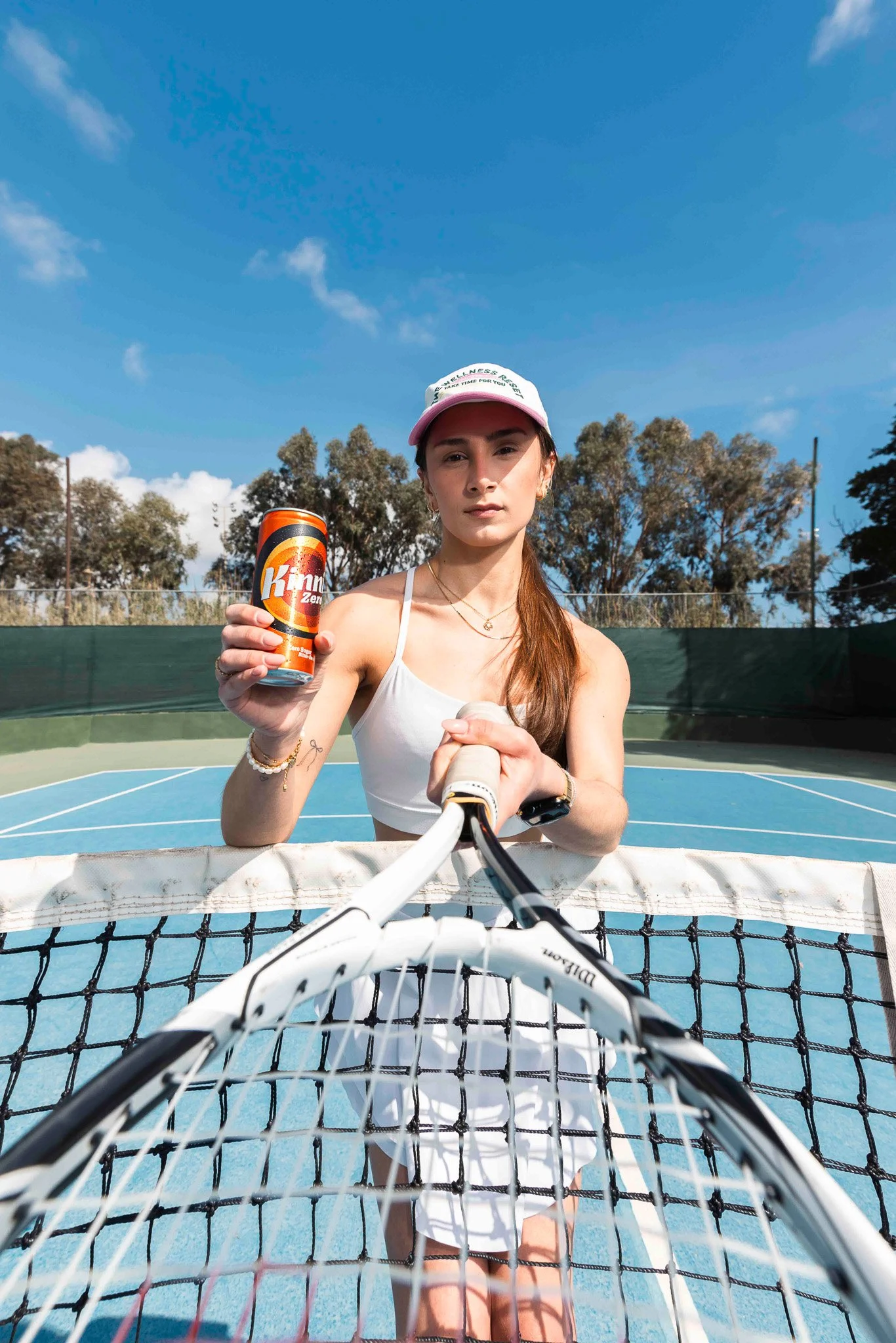 woman with tennis racket and holding a kinnie can, distorted image outdoors on a tennis court
