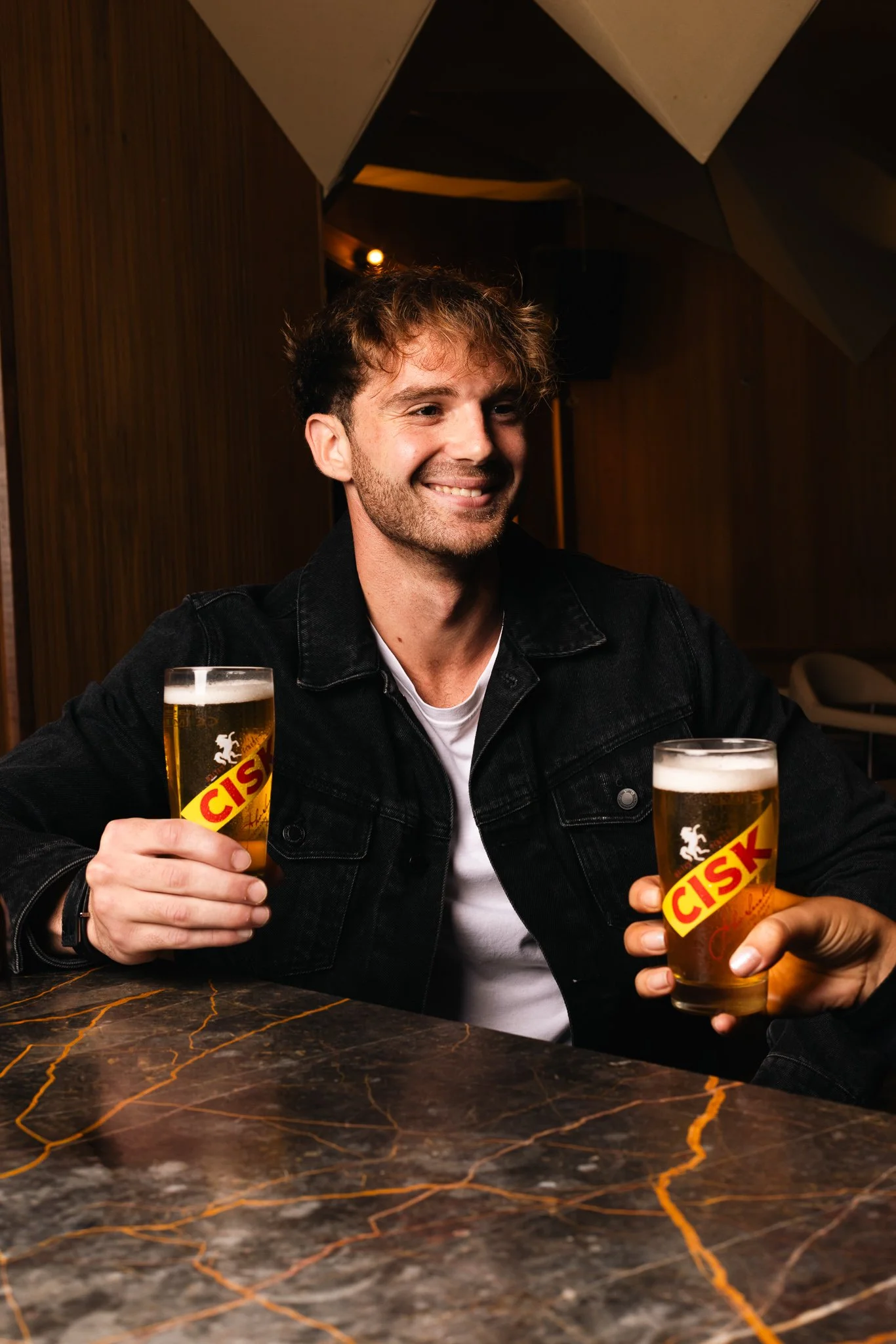 man holding a cisk glass indoors, winter photoshoot