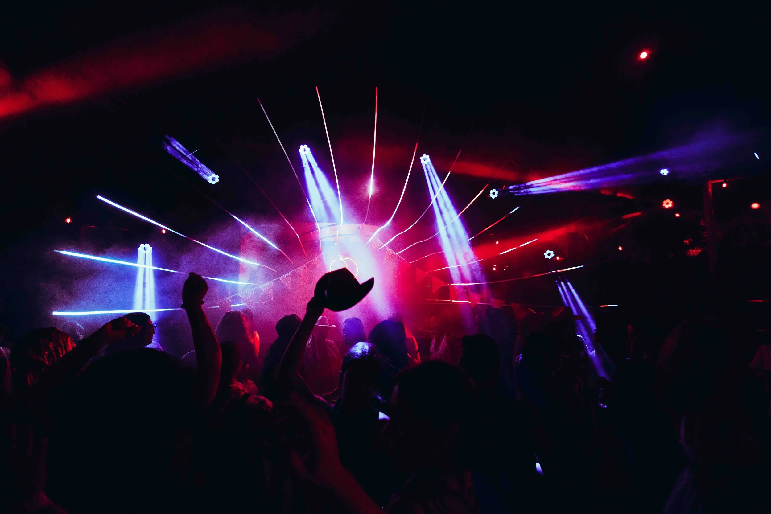 A concert scene with colorful laser lights, fog, and a crowd of people dancing and enjoying the show.