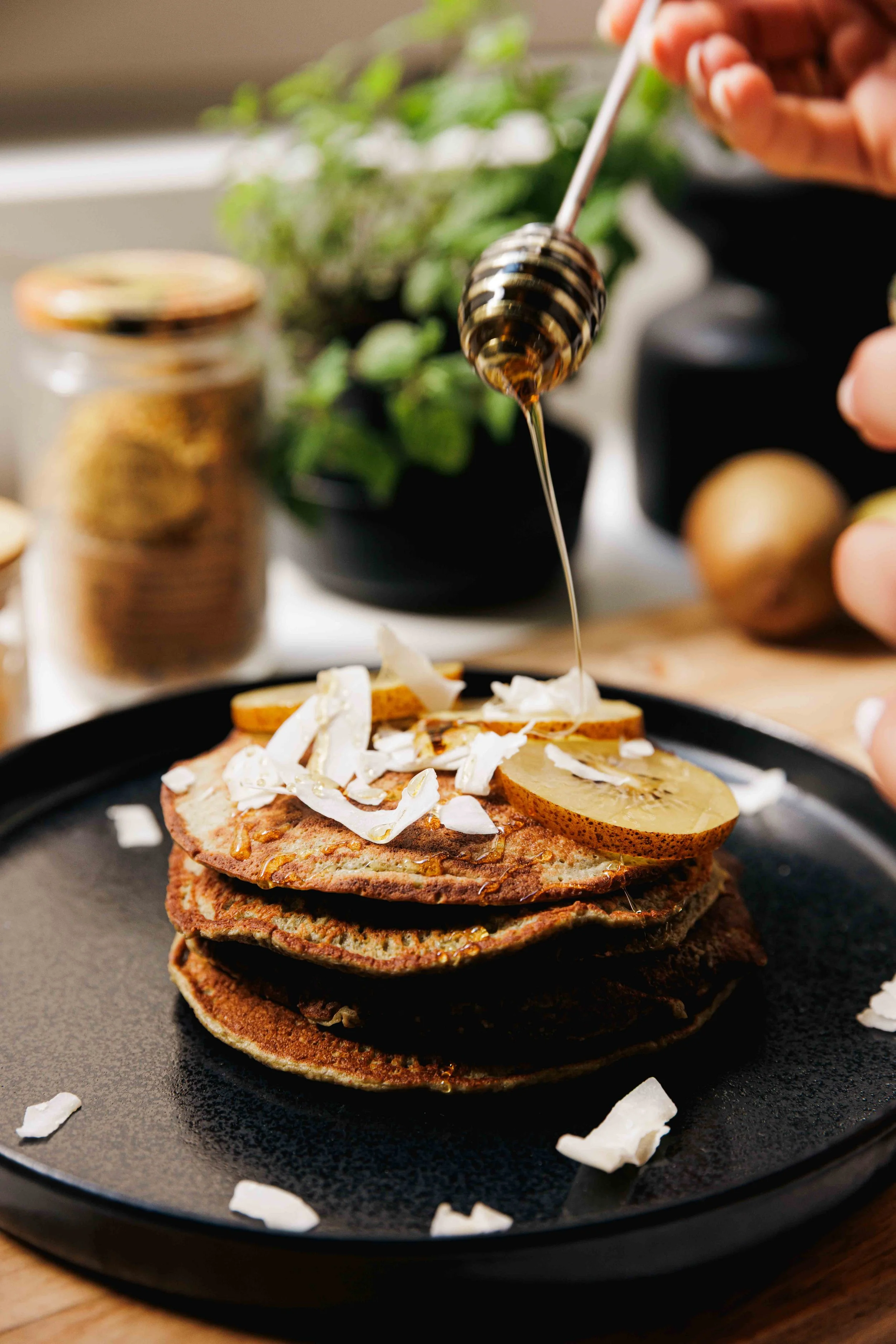 honey being drizzled on a healthy stack of pancakes with kiwi
