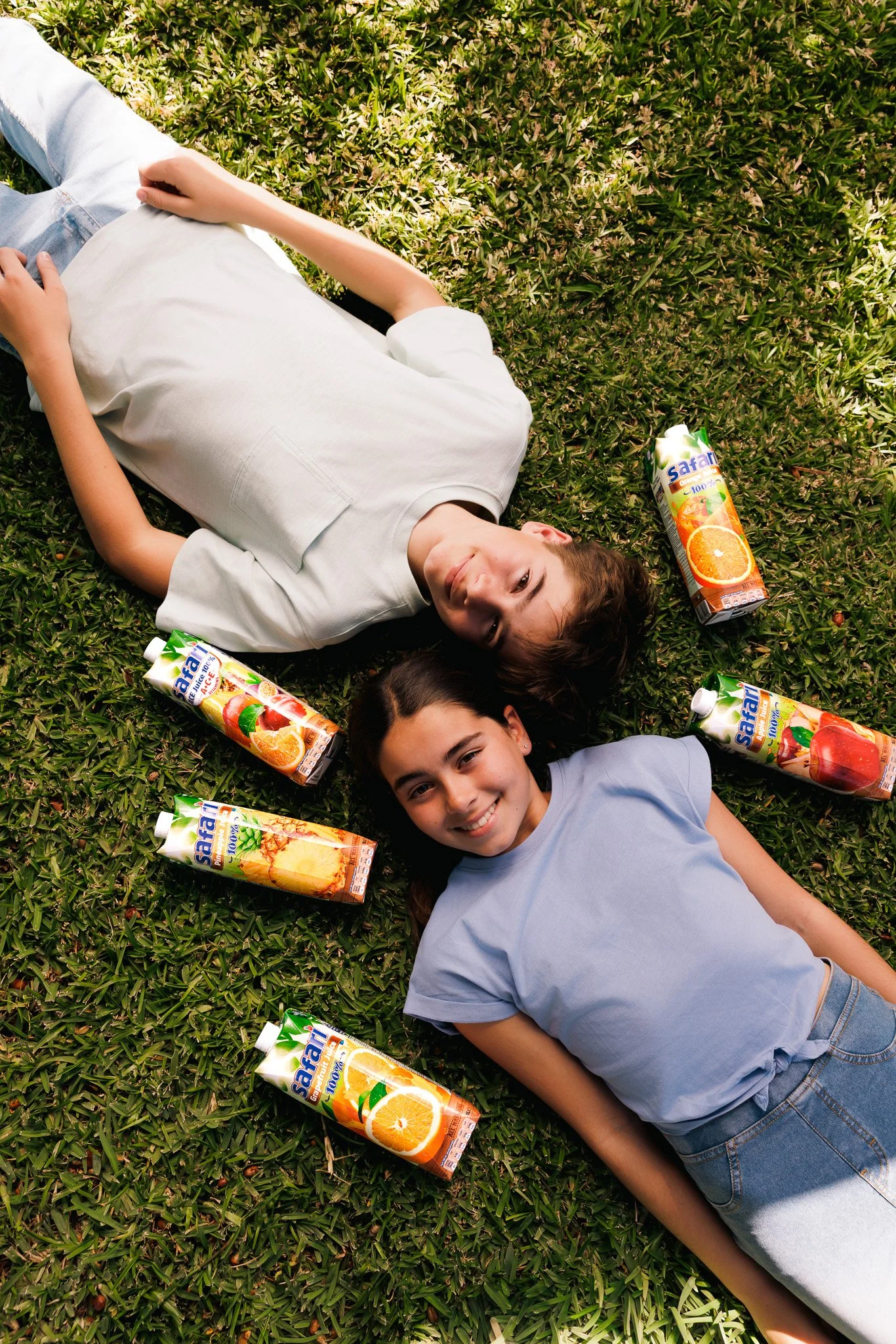 two kids laying flat on the grass, surrounded by different flavours of safari juice boxes