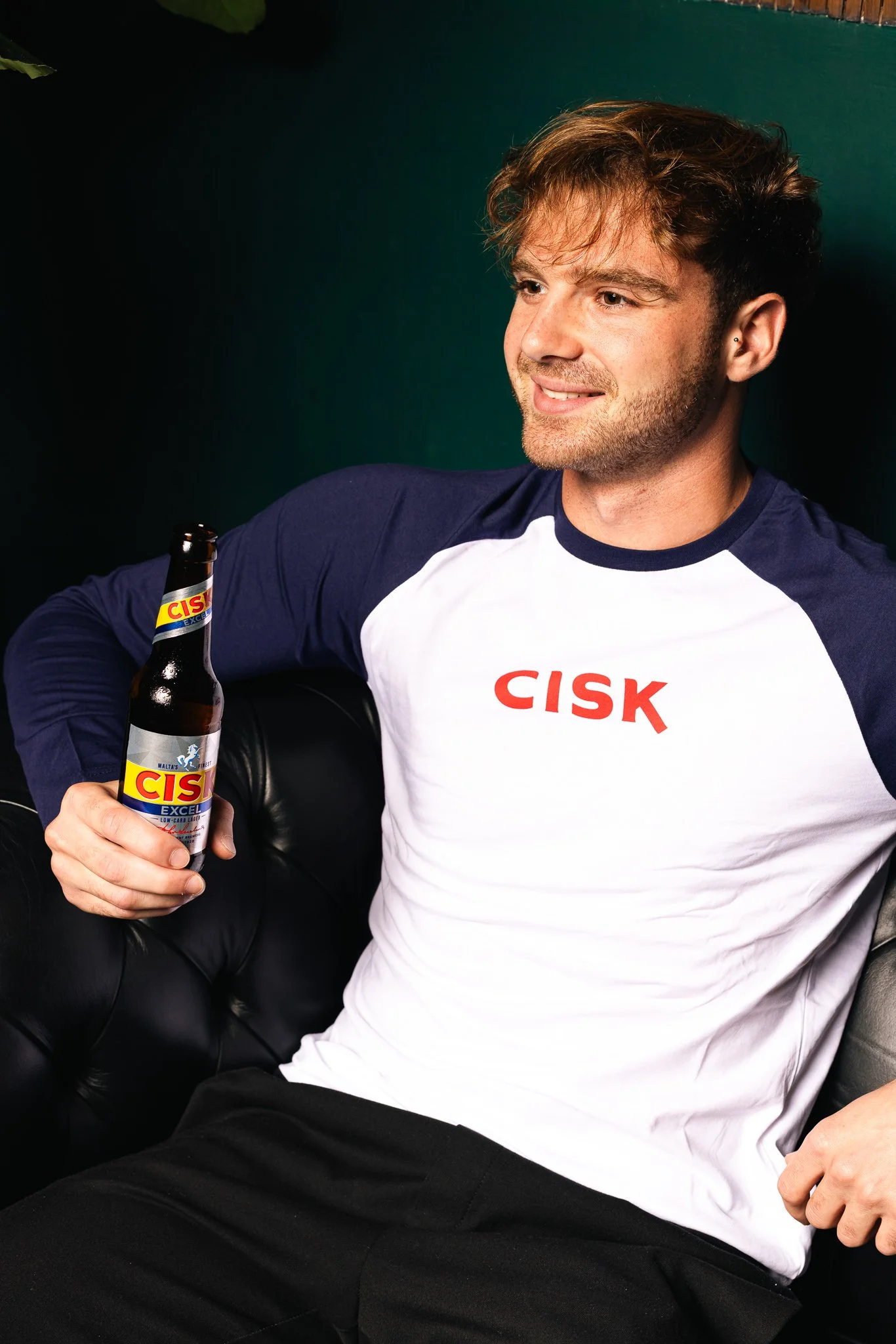 man wearing a cisk long sleeve top in navy, holding a cisk excel bottle, smiling