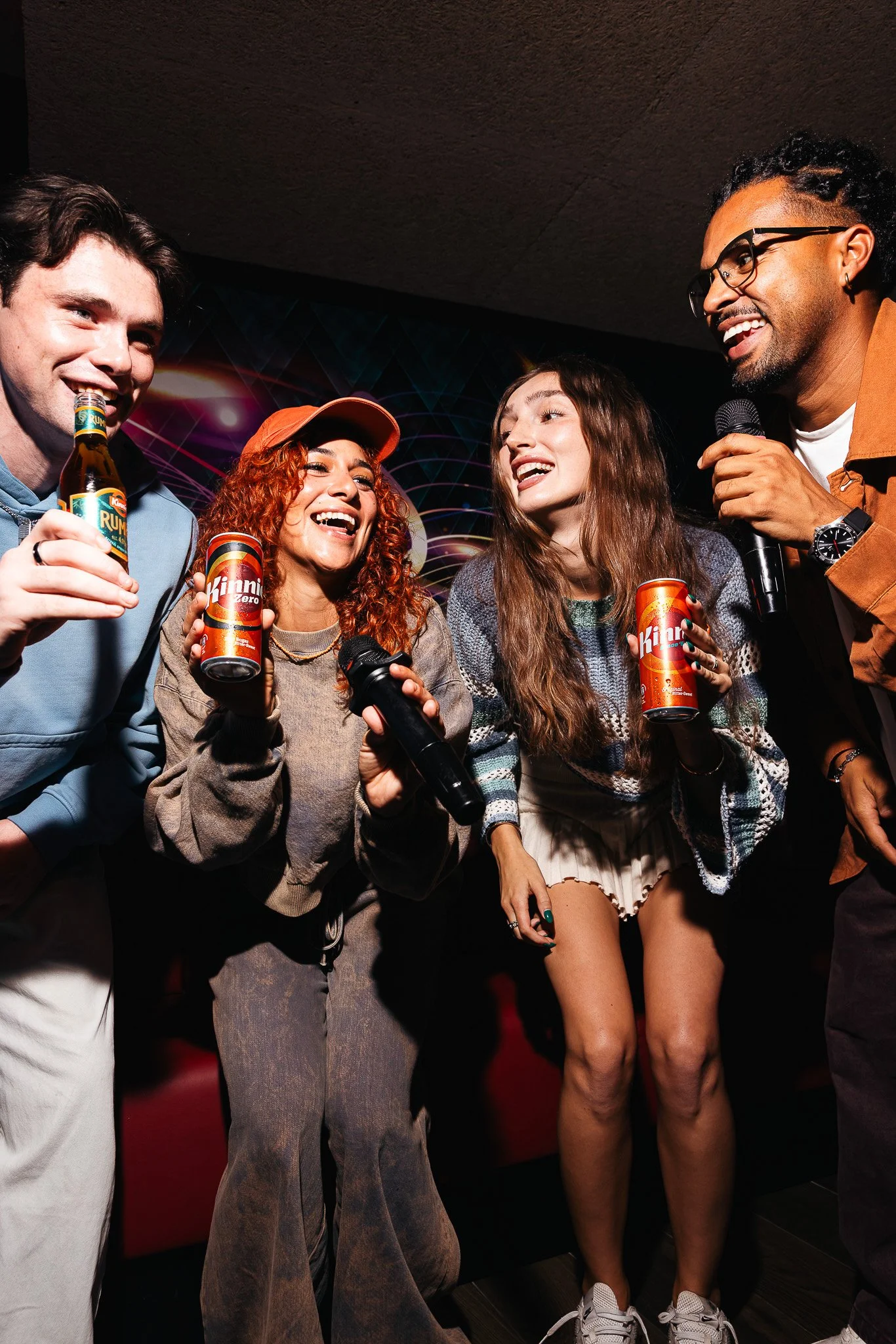 group of friends indoors singing karaoke, everyone holding a can of Kinnie, photography
