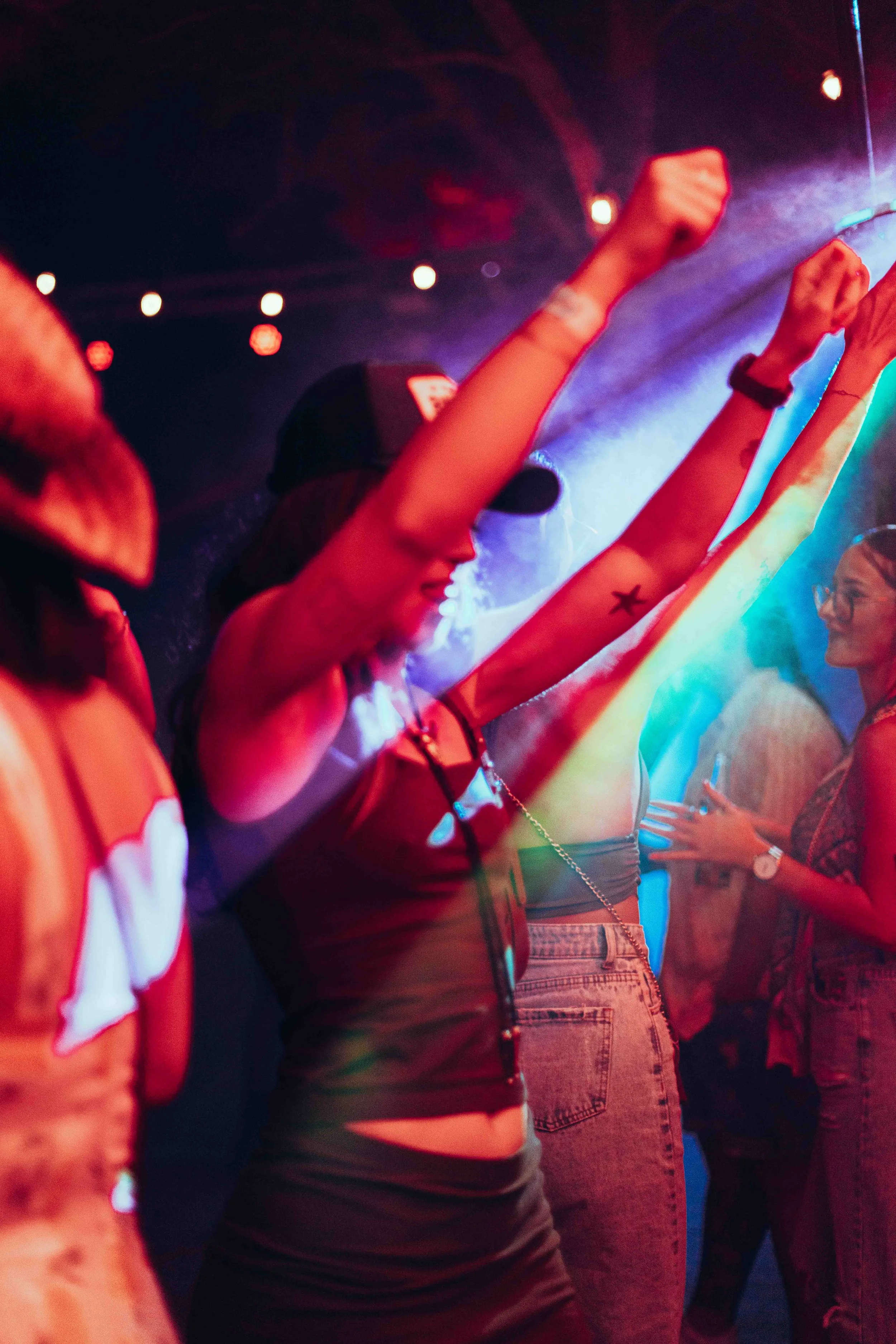 Crowd of young people dancing at a nightclub or concert with colorful lighting.