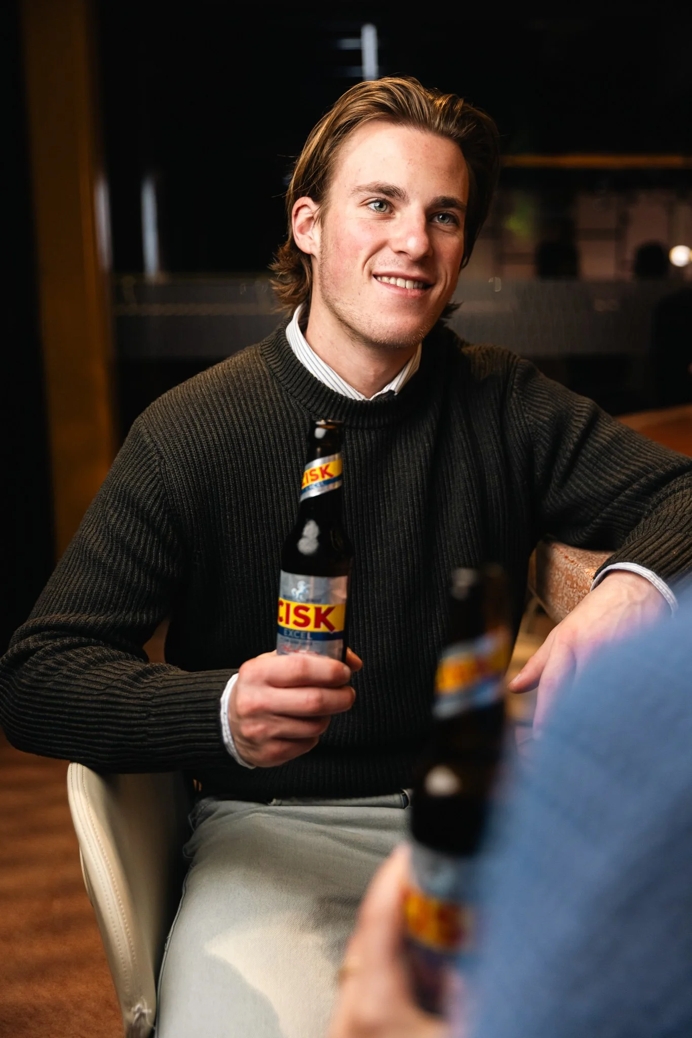 man holding a cisk excel bottle indoors, winter, photoshoot