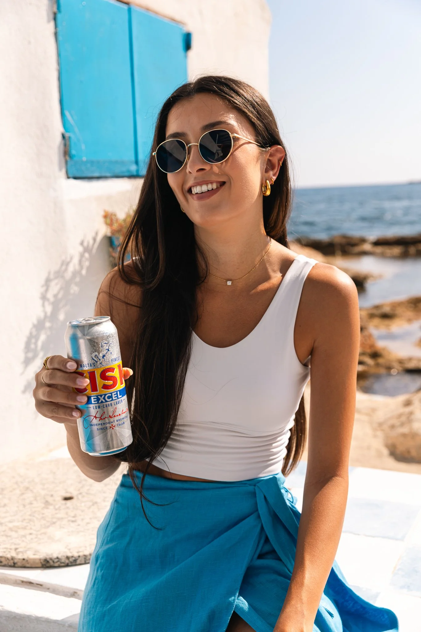 woman by the beach, wearing blue and holding a cisk excel can