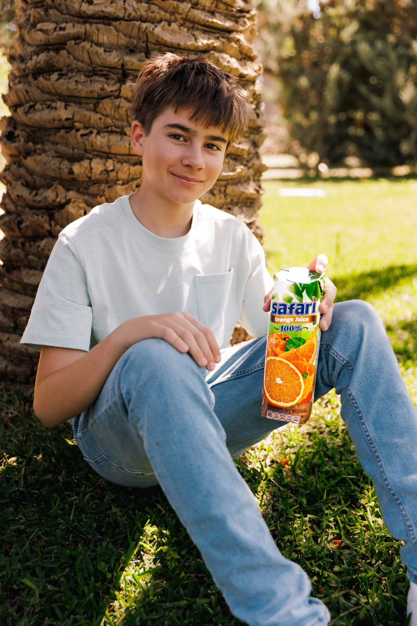 young boy holding a safari orange juice box in hand, sitting down on grass