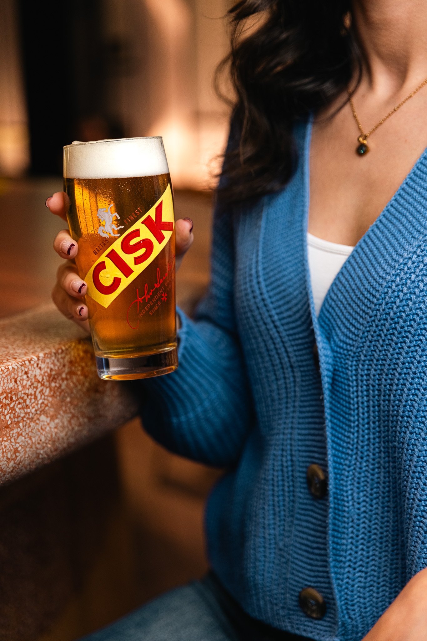 woman holding a cisk glass at a bar, indoors, winter