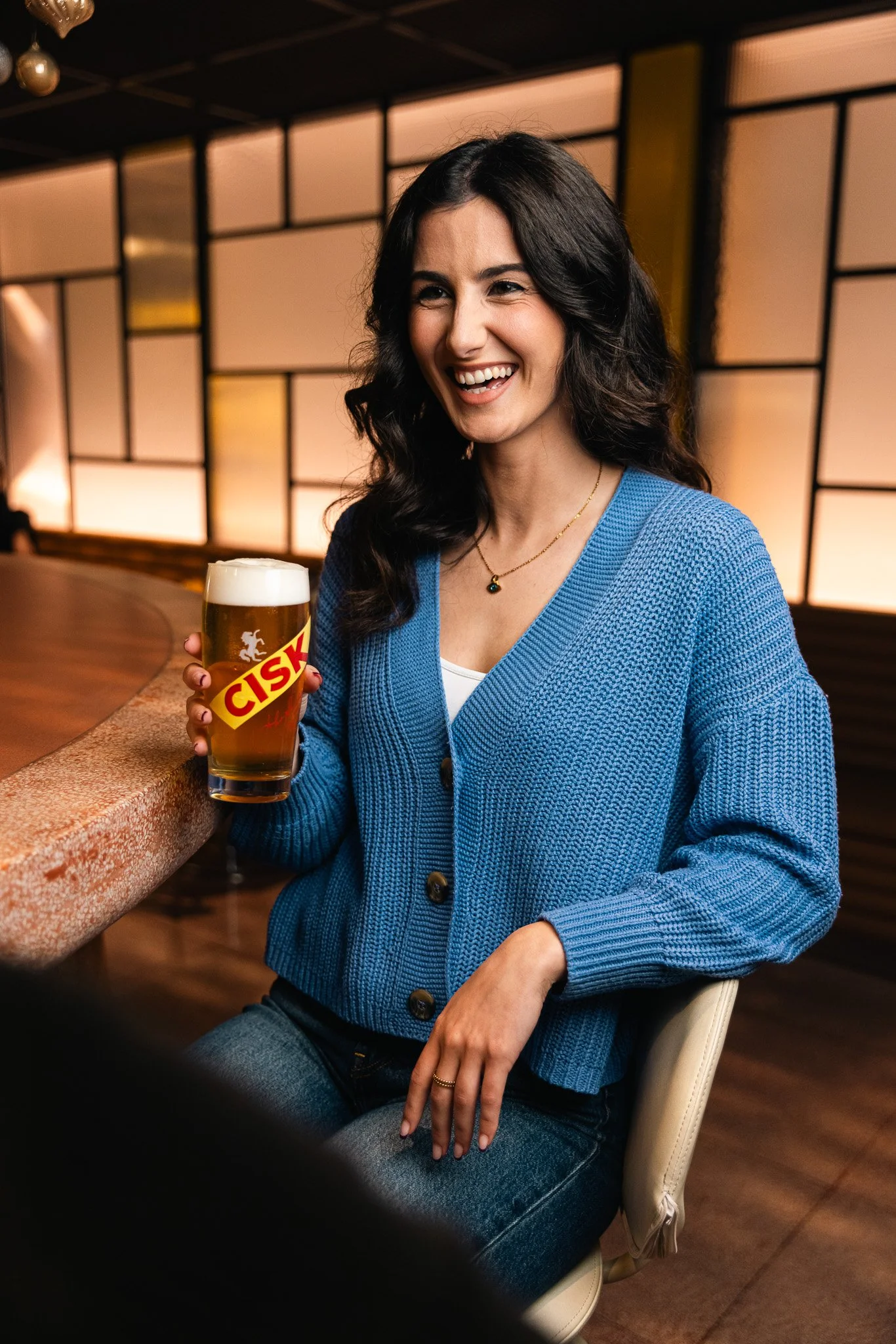 woman holding a cisk glass at a bar, smiling