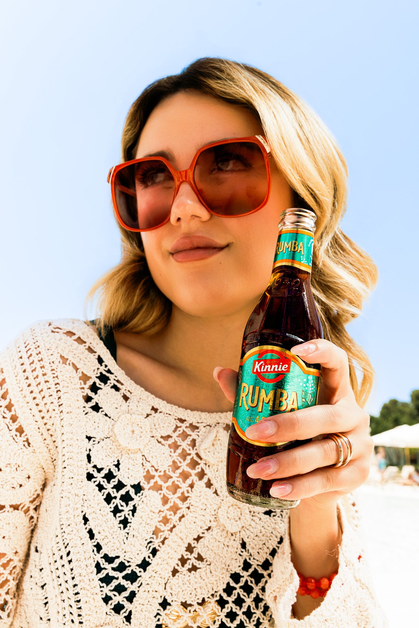 woman with big orange sunglasses outdoors, holding a kinnie rumba bottle