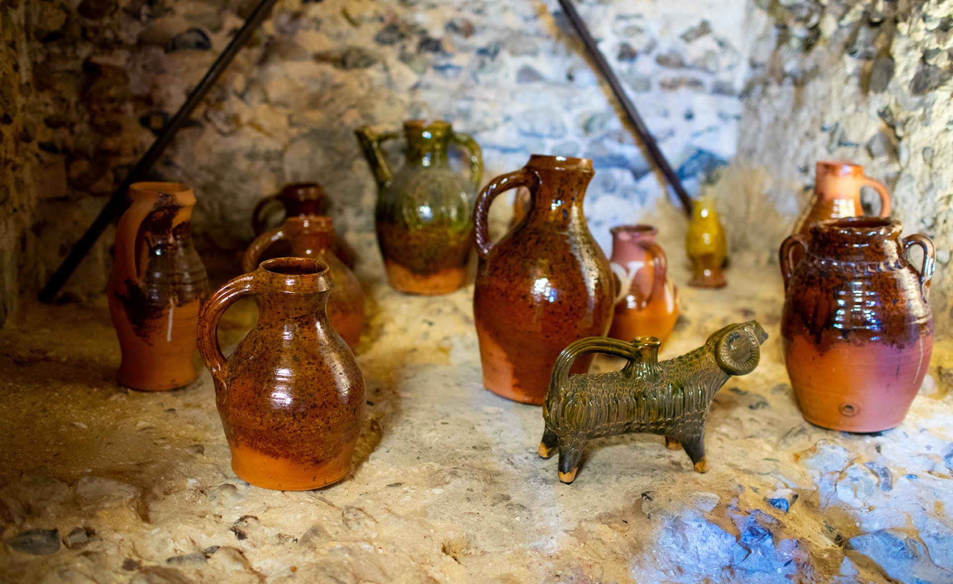 Collection of ceramic pottery and jugs displayed on a rustic stone surface, including items with earthy tones and a ram-shaped pottery piece in the foreground.