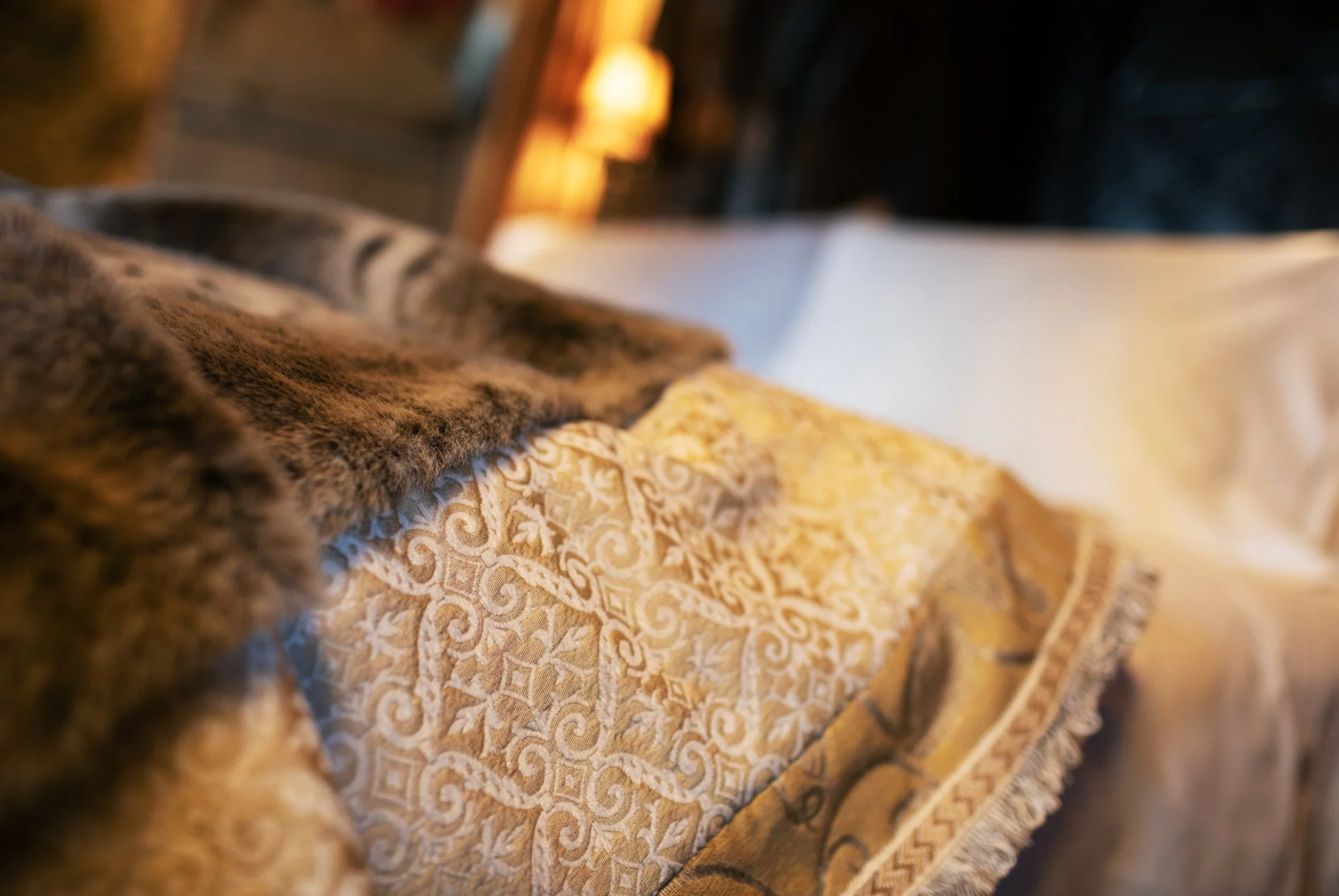 Close-up of a luxurious bed with a decorative, patterned blanket and a fur throw, white pillow in the background.