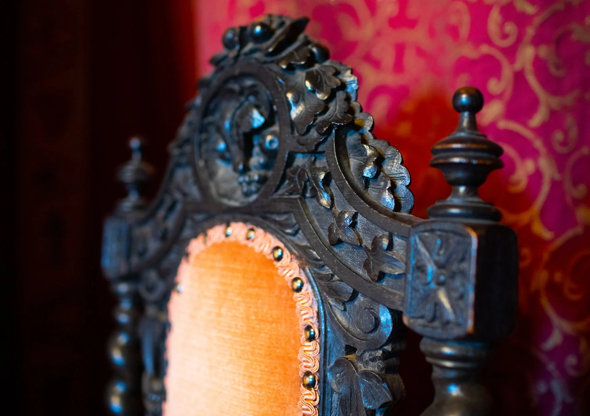 Ornate wooden chair back with intricate carvings against red patterned background.