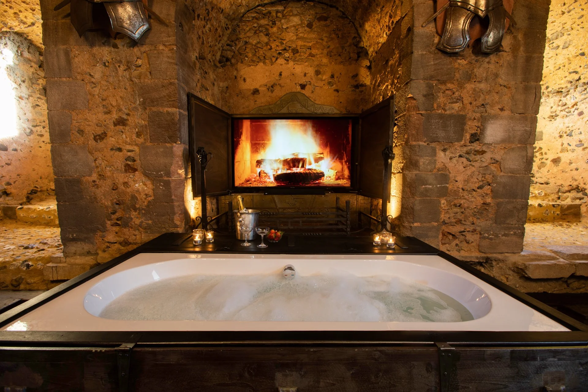 Luxurious stone room with a fireplace and bathtub, candles, and champagne.