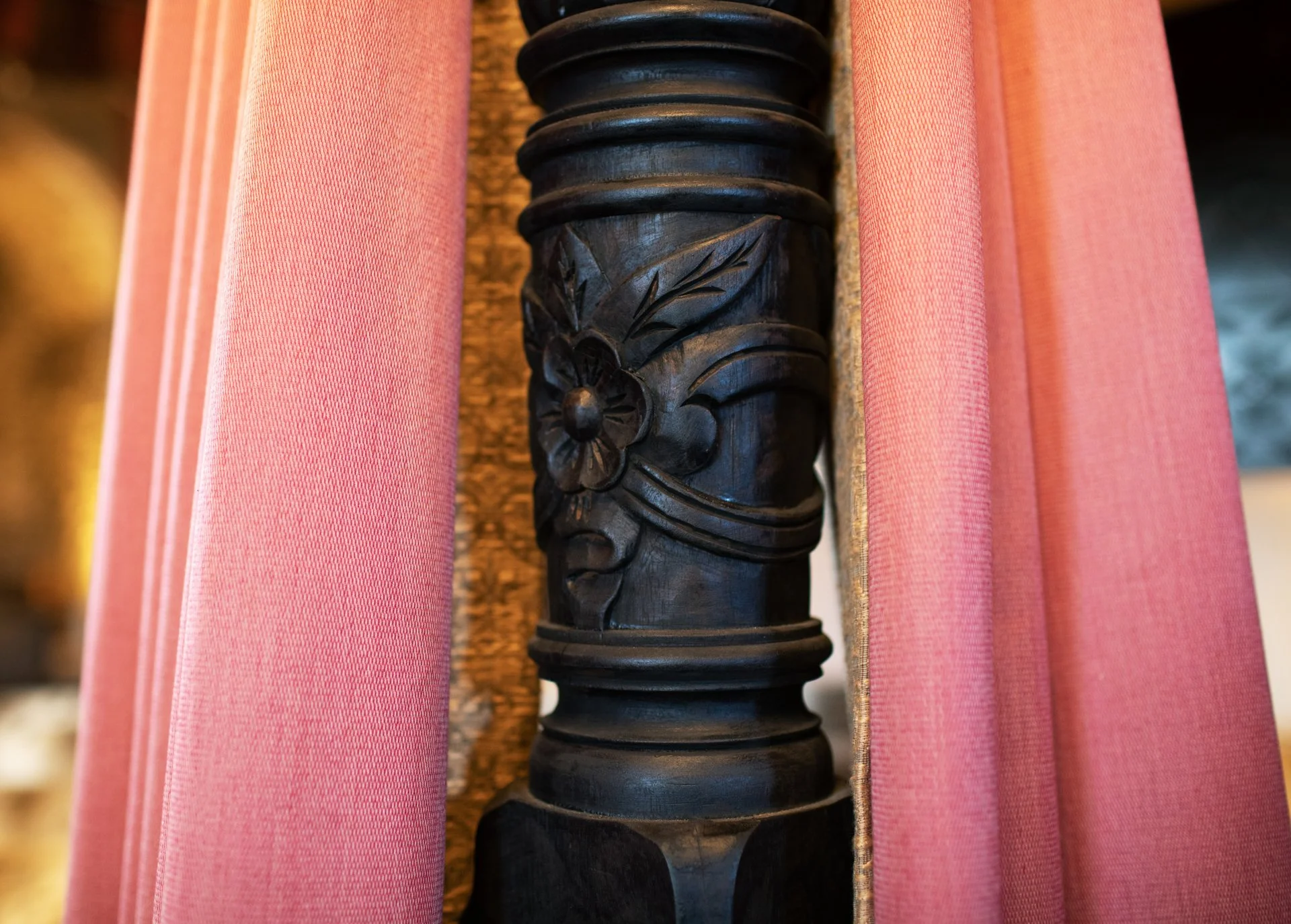 Close-up of a carved wooden post with floral design, surrounded by pink fabric drapes.