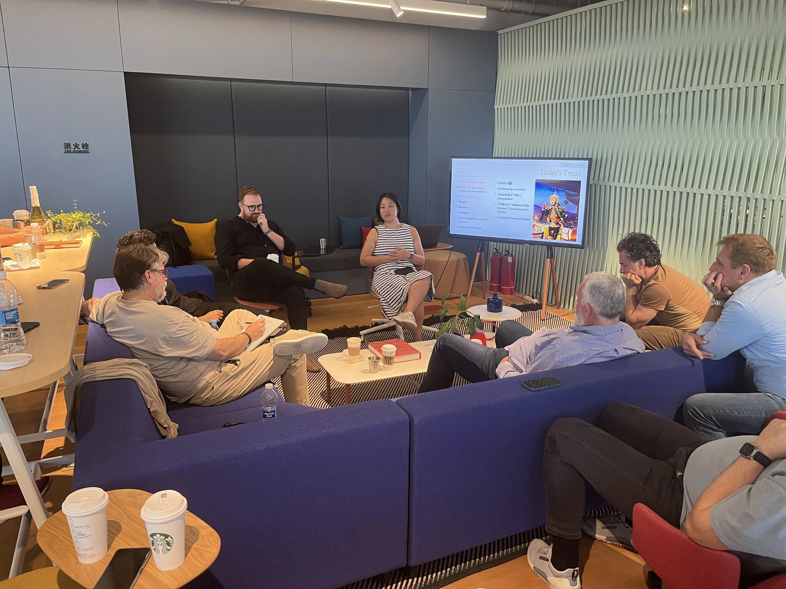 A group of 6 people sitting down, talking and listening to the presentation