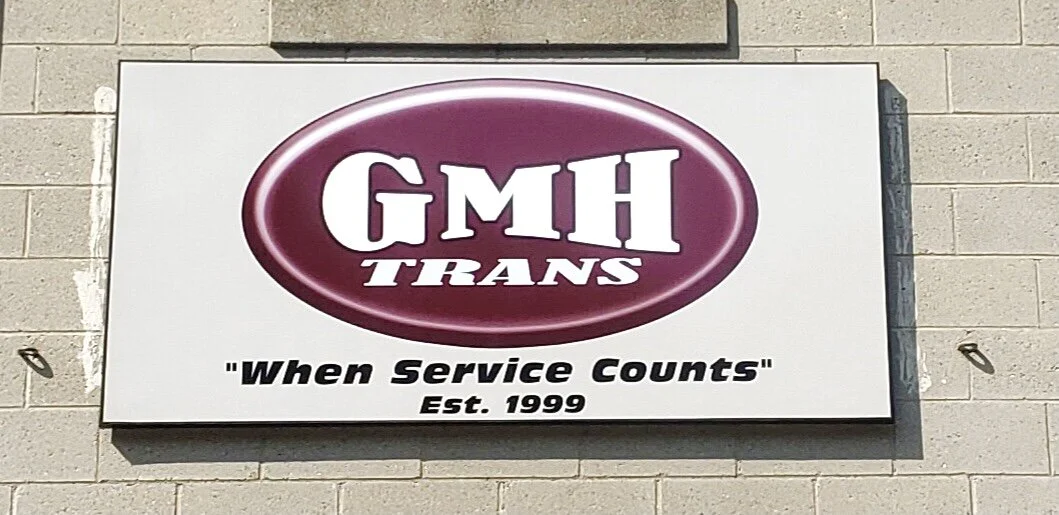 Sign for GMH Trans with the slogan 'When Service Counts' and established date 1999, mounted on a beige brick wall.