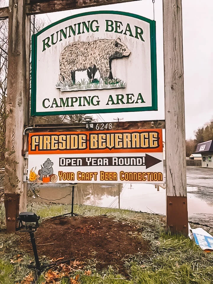 Sign for Running Bear Camping Area with black bear illustration, advertising fireside beverages and craft beer to be available year-round.