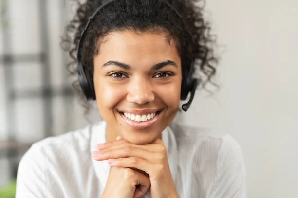 Headshot of friendly African American millennial woman in a headset sitting with her hands on a chin, working in the customer service department as call center operator, helping client with inquiry