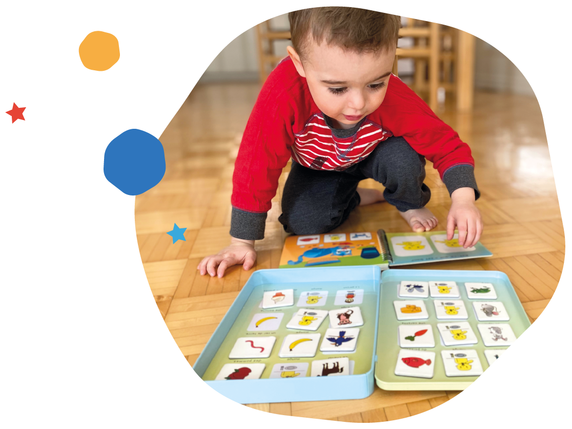 Un jeune garçon en train de jouer avec des cartes illustrées sur un sol en parquet. L'aire de jeu est composée de deux boîtes contenant des cartes avec des images d'animaux et d'objets.