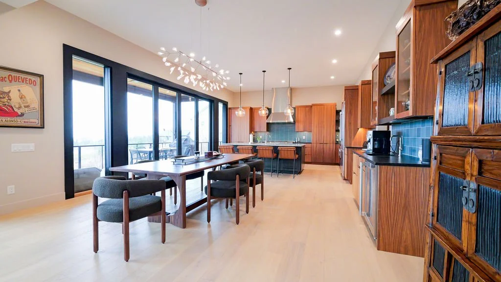 Open-concept kitchen and dining area with large sliding glass doors, wooden cabinetry, a dining table with six chairs, and modern pendant lighting.