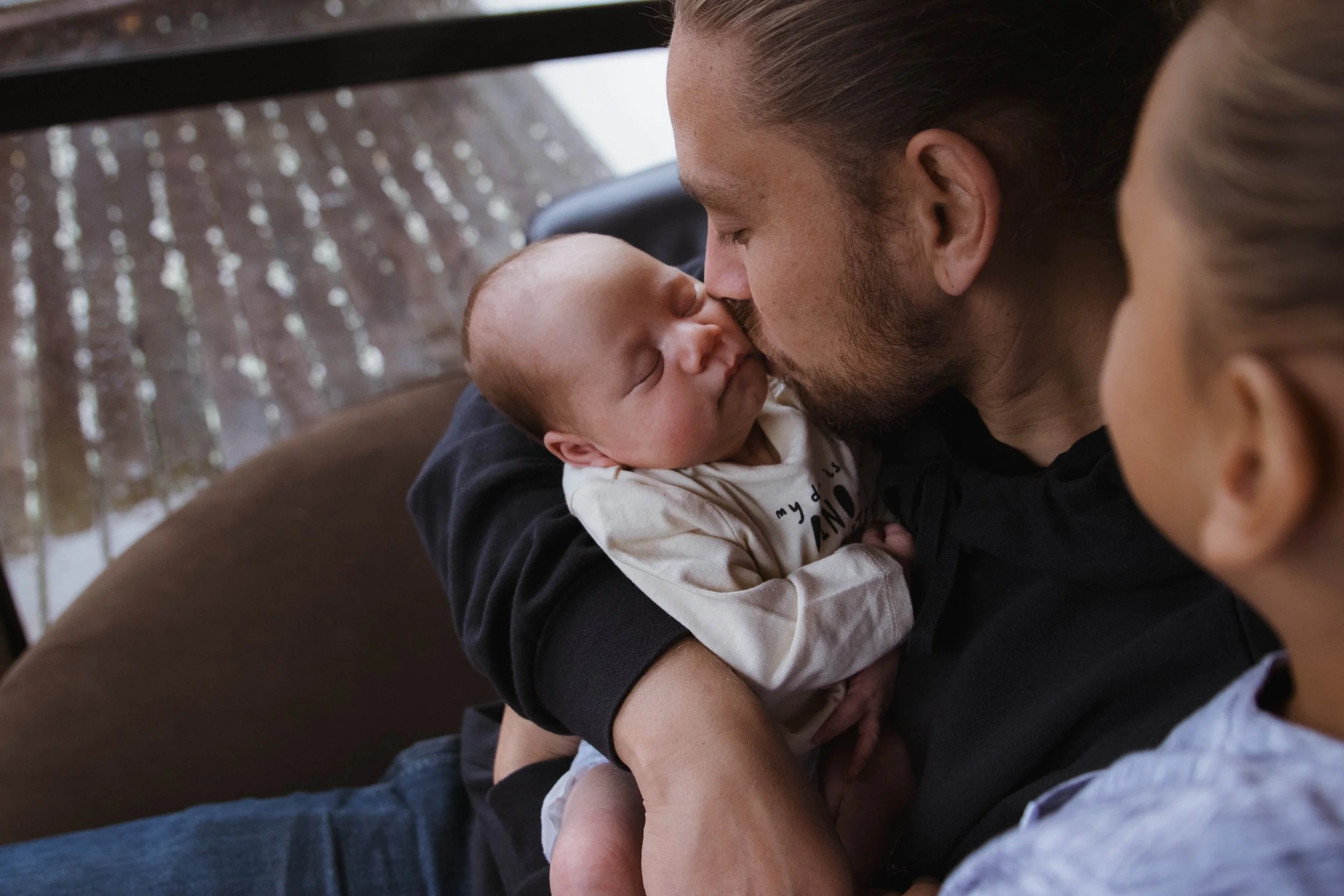 A father holding his newborn baby, with his older son looking on.