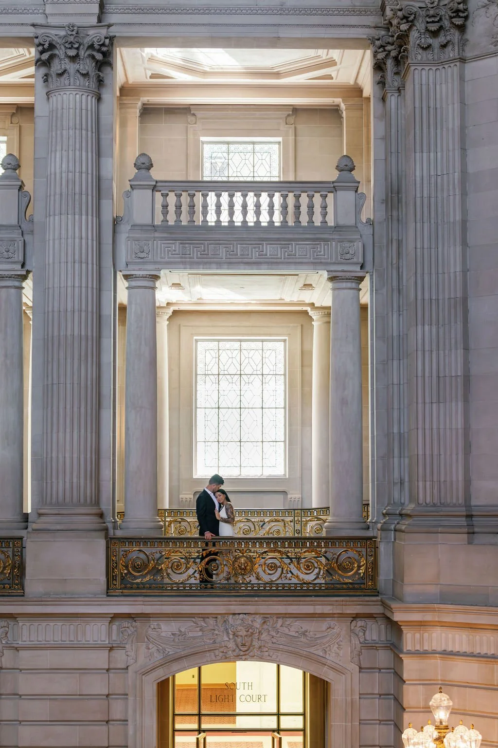 A newlywed couple walking out of San Francisco city hall, celebrating with friends and family who are throwing streamers. The bride is holding a bouquet and wearing a white wedding dress, and the groom is dressed in a black tuxedo.