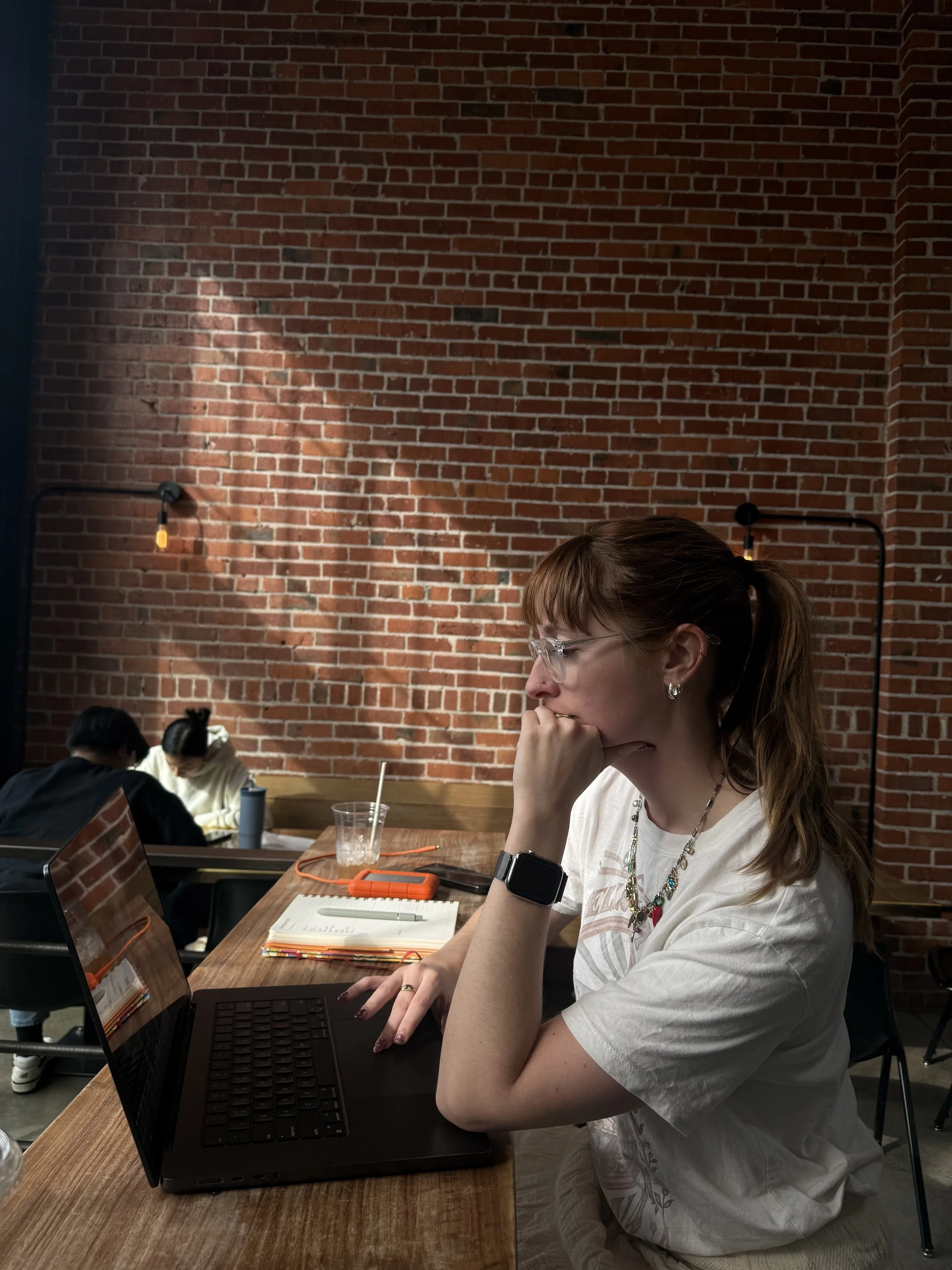 A young woman with glasses and a necklace sitting at a wooden table working on a laptop in states coffee in martinez, california 