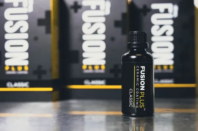 A black bottle labeled "Fusion Plus Ceramic Coating Classic" in front of black boxes with white and yellow lettering, likely automotive or detailing products.