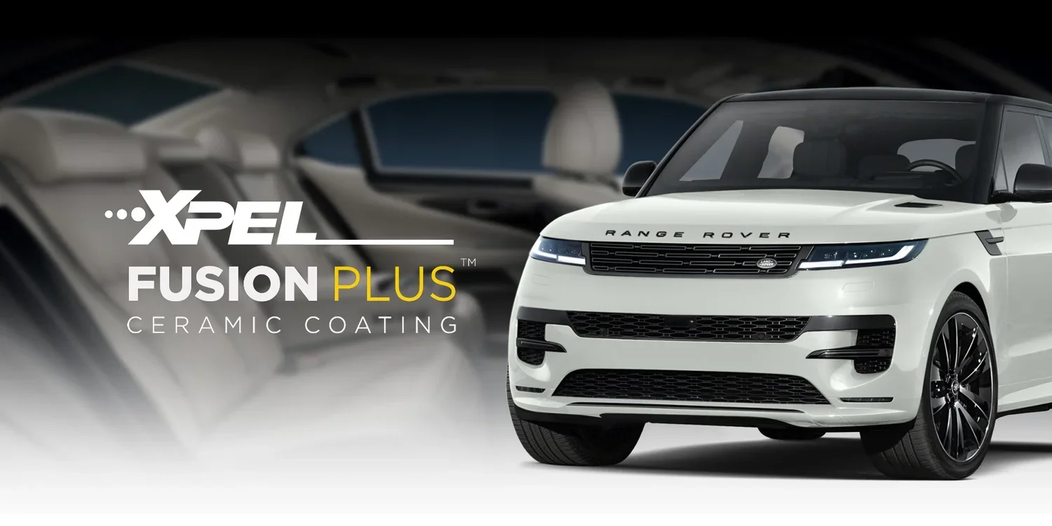 White Range Rover vehicle with black wheels and front grille, advertising XPEL Fusion Plus ceramic coating, with a blurred background of interior seats.