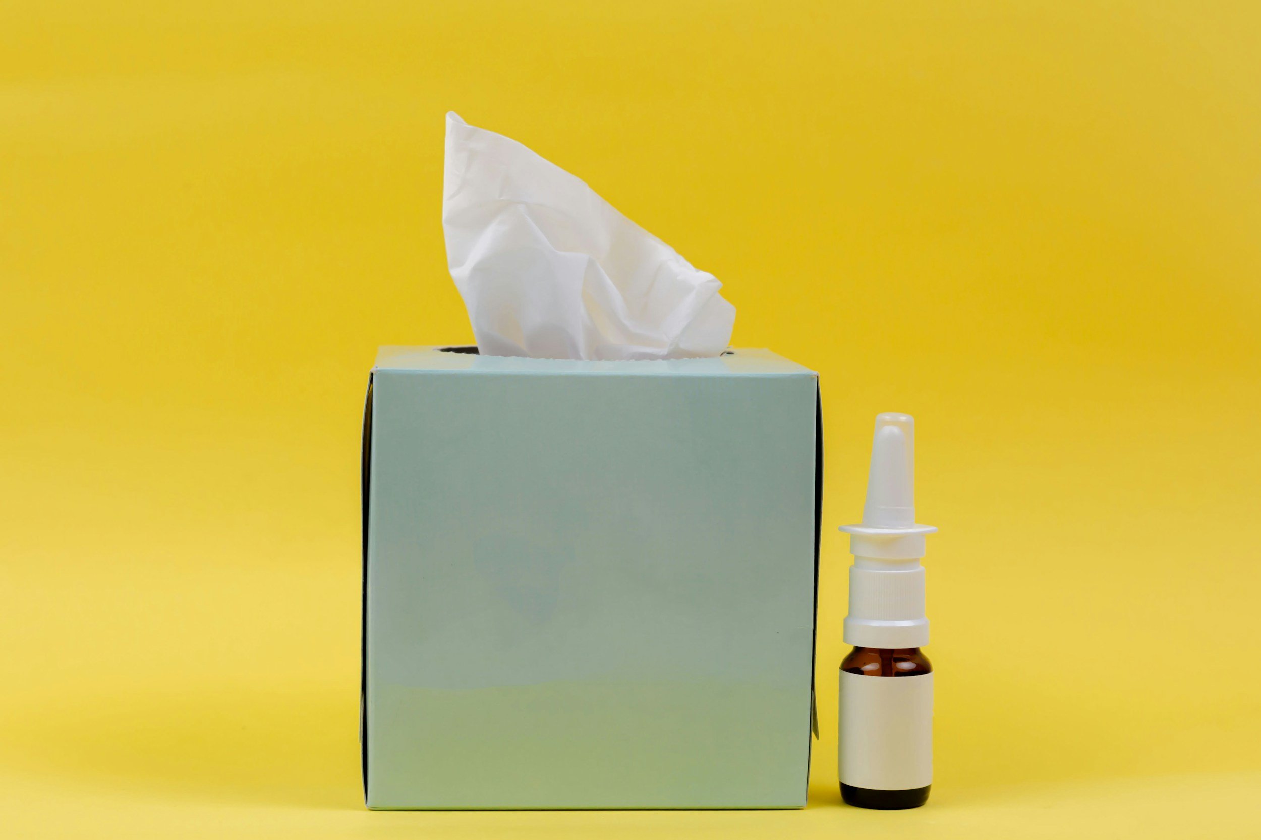 A square box of tissues next to nasal spray.