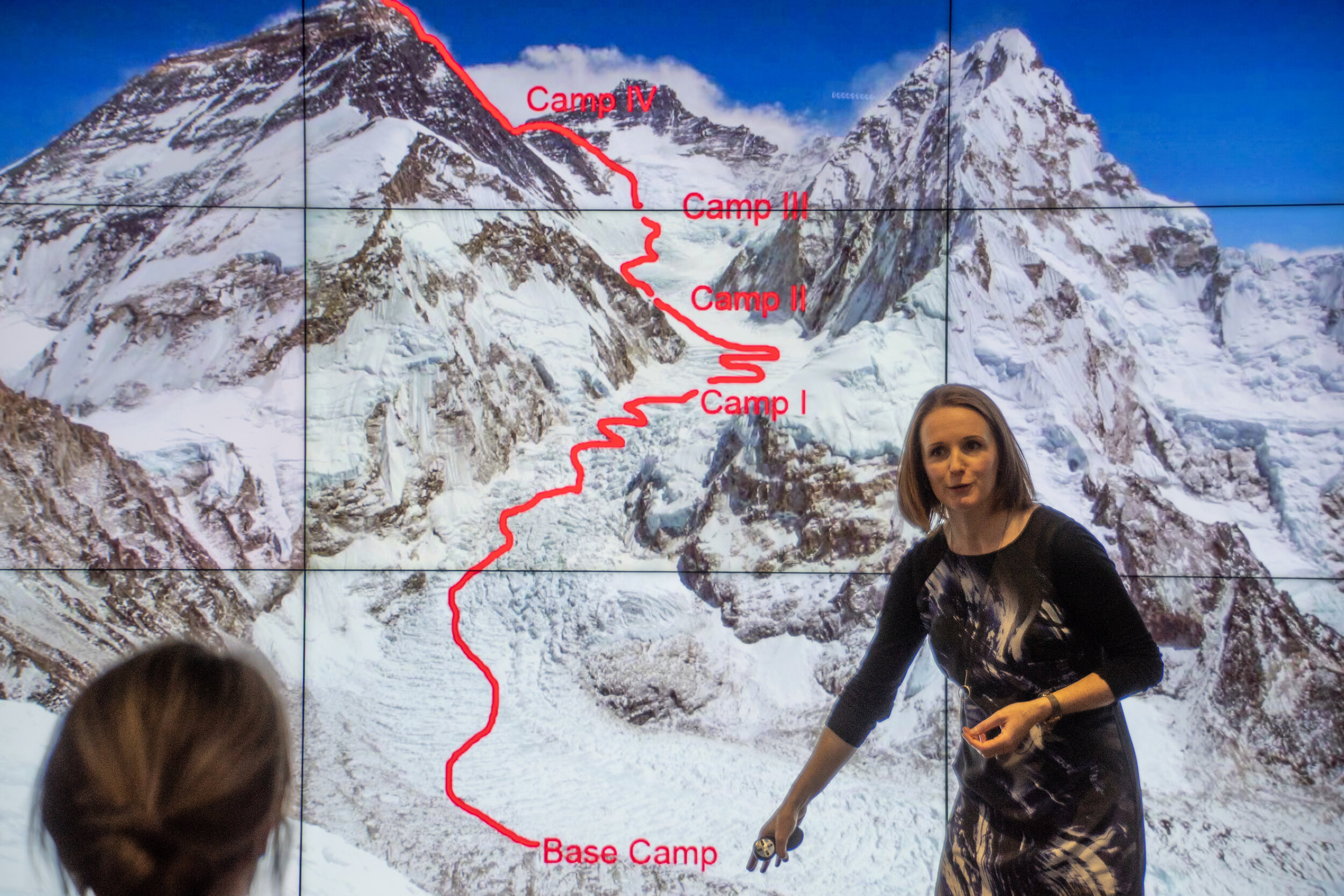 Tori James stands on stage at Duke of Edinburgh event presenting infront of an image of the route to Everest.