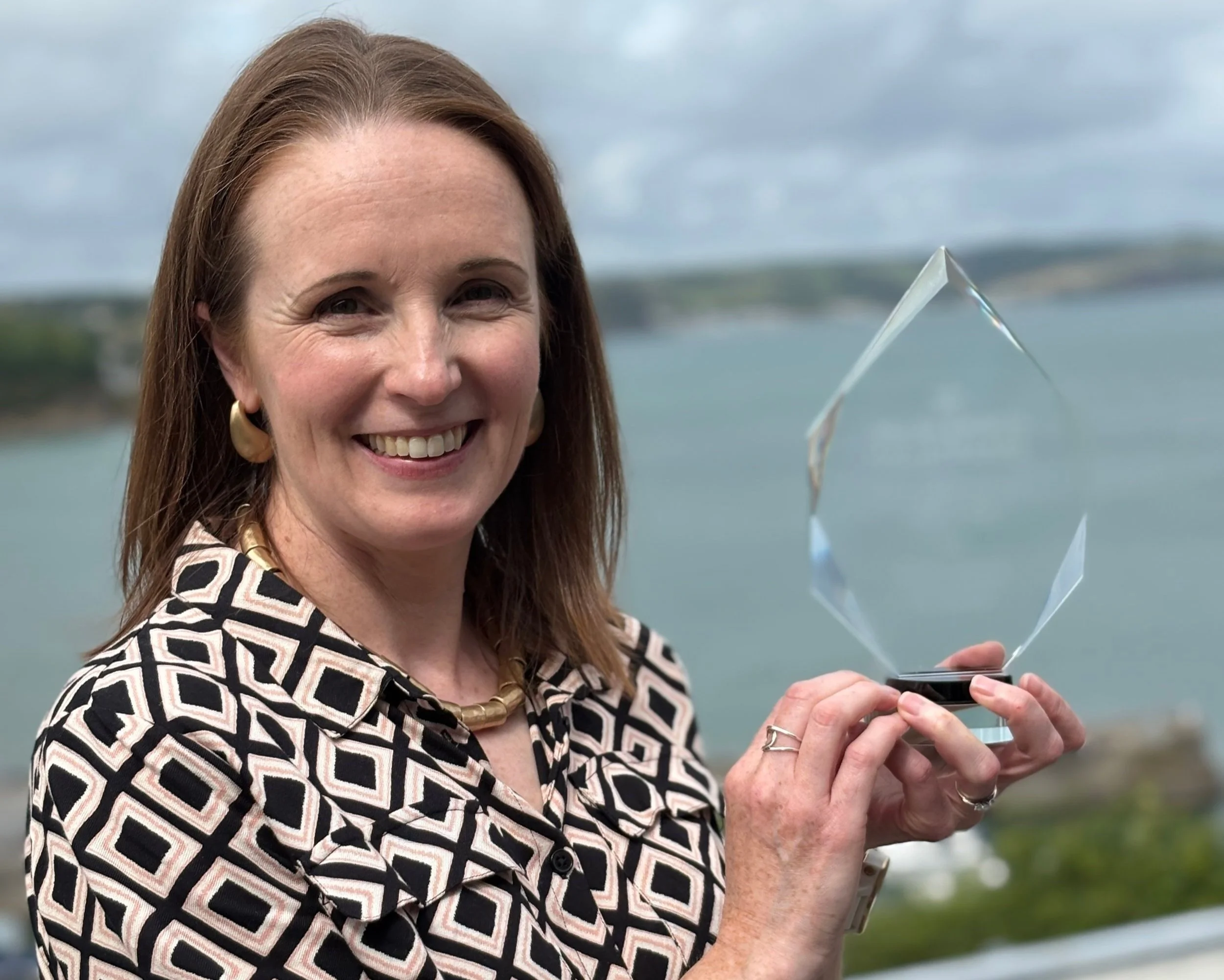Tori James stands infront of the sea holding a Welsh Sport Hall of Fame award.