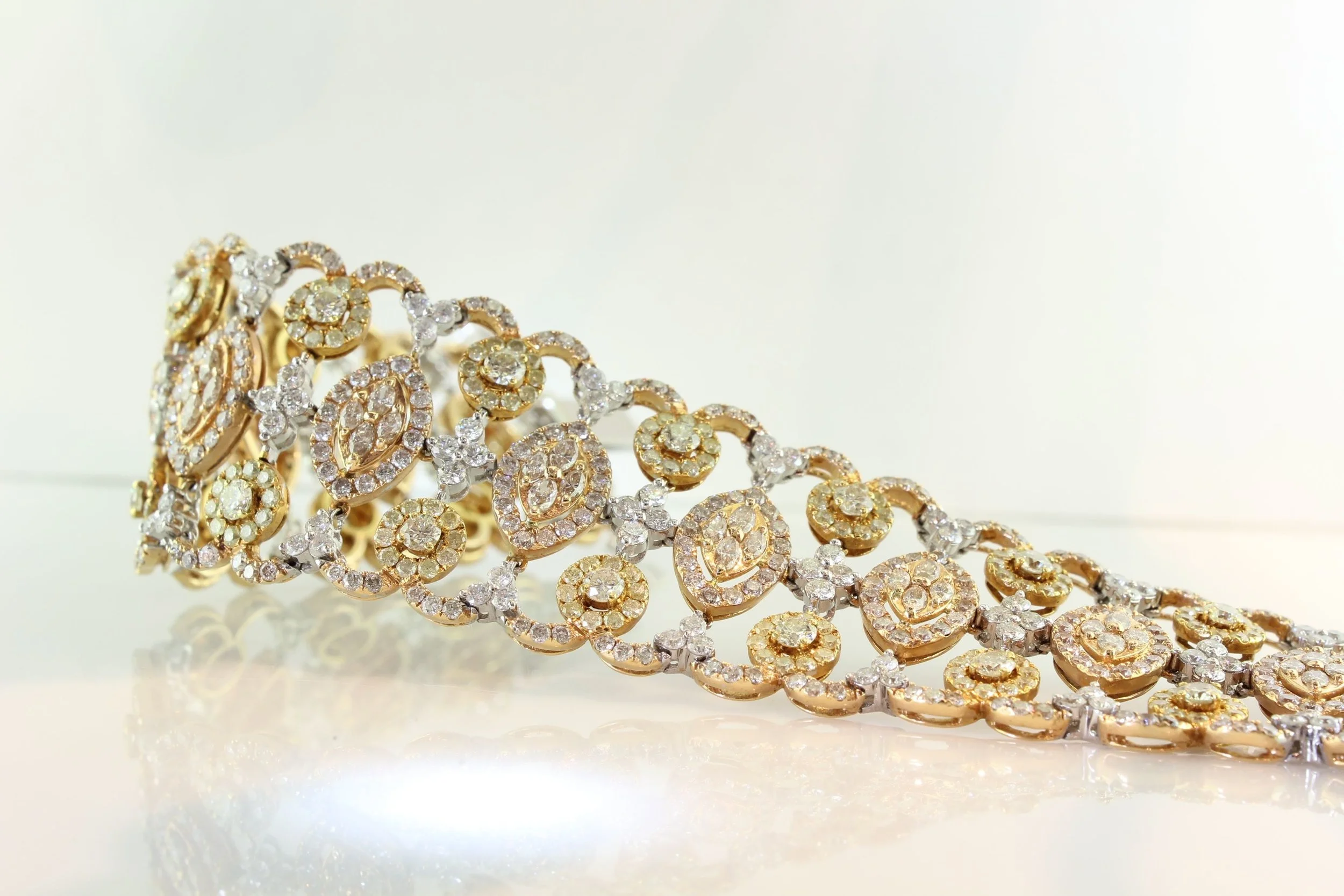 A gold and silver bracelet adorned with numerous small diamonds, intricately designed with swirling patterns.