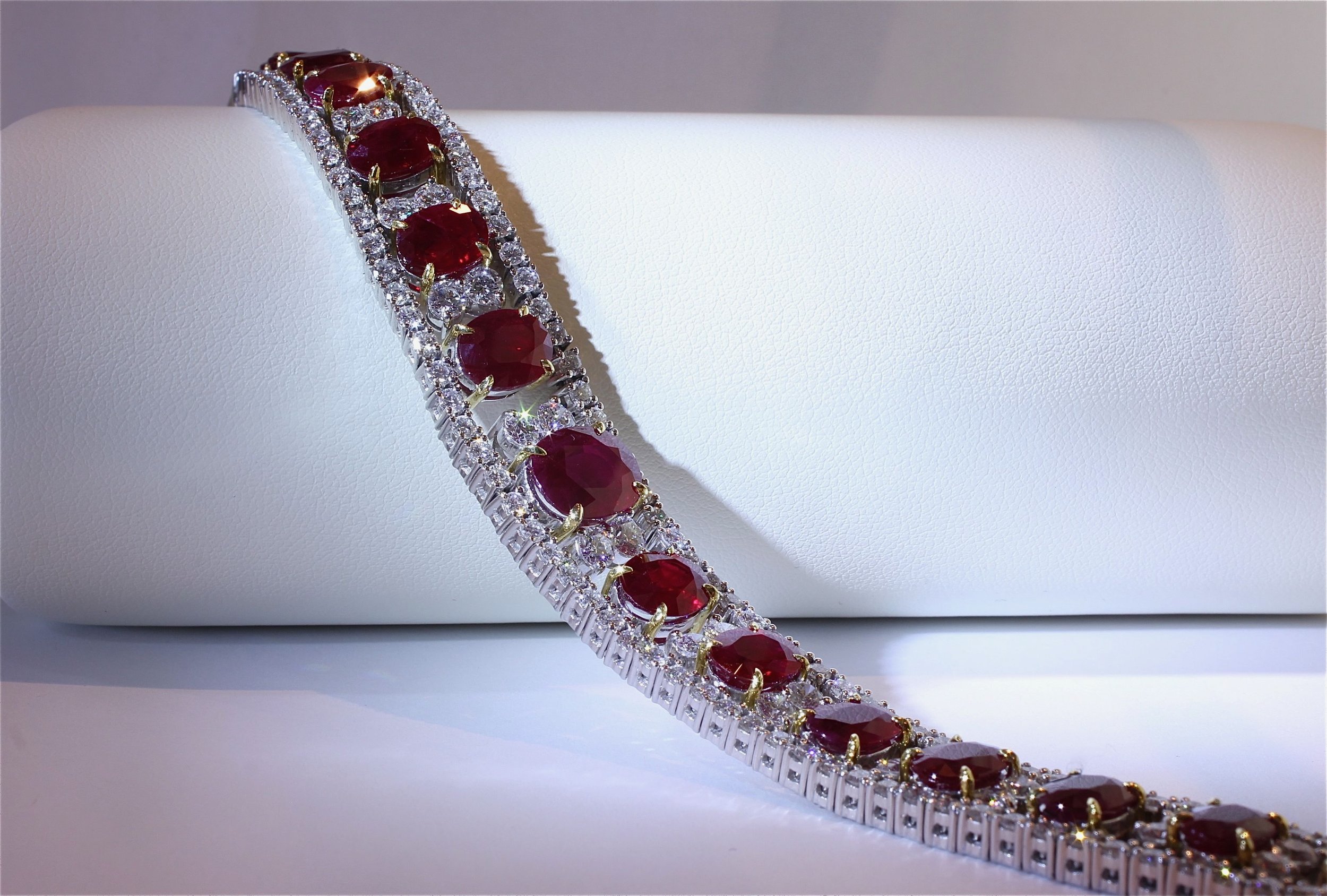 A silver bracelet with large oval-shaped red gemstones and small clear diamonds, displayed on a white surface.