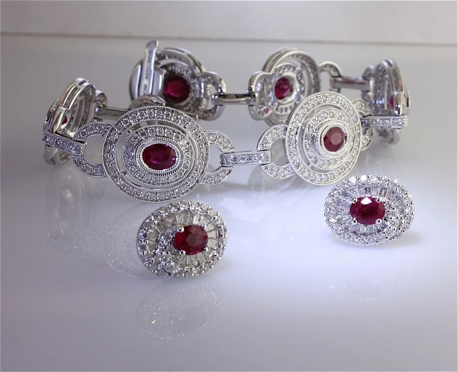 A collection of silver jewelry with red gemstone accents, including a bracelet, earrings, and a ring, displayed on a reflective surface.