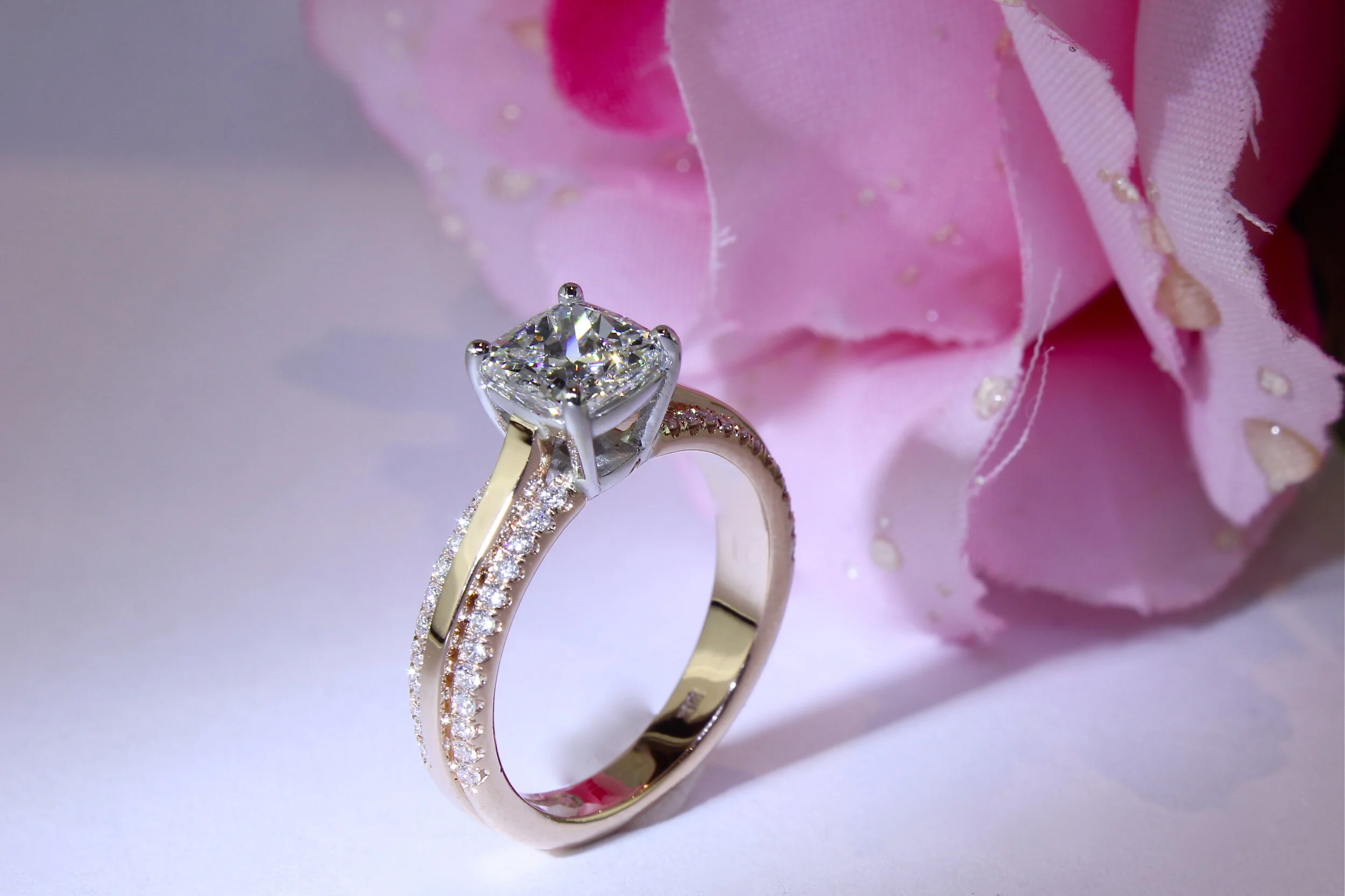 Close-up of three rings, with a large diamond ring in the middle and two matching bands decorated with small diamonds on each side, placed in front of a pink fabric with floral design.